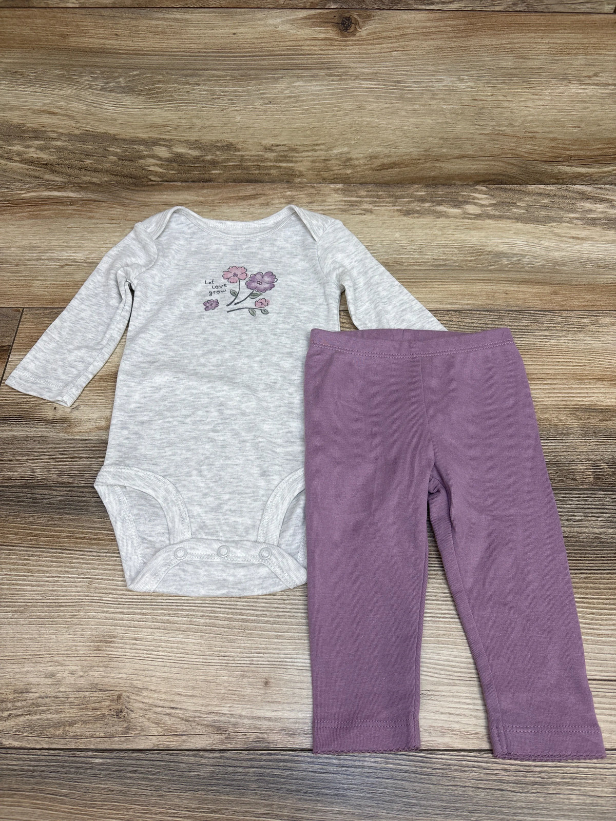 Front view of Carter’s 2pc Let Love Grow bodysuit and pants set showcasing a floral graphic and coordinating colors on a wood surface