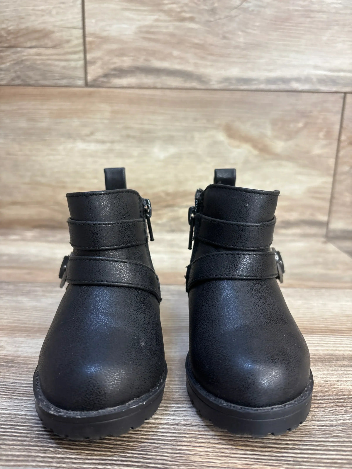 Black toddler boots with side zippers and buckle straps, kids footwear on wood floor