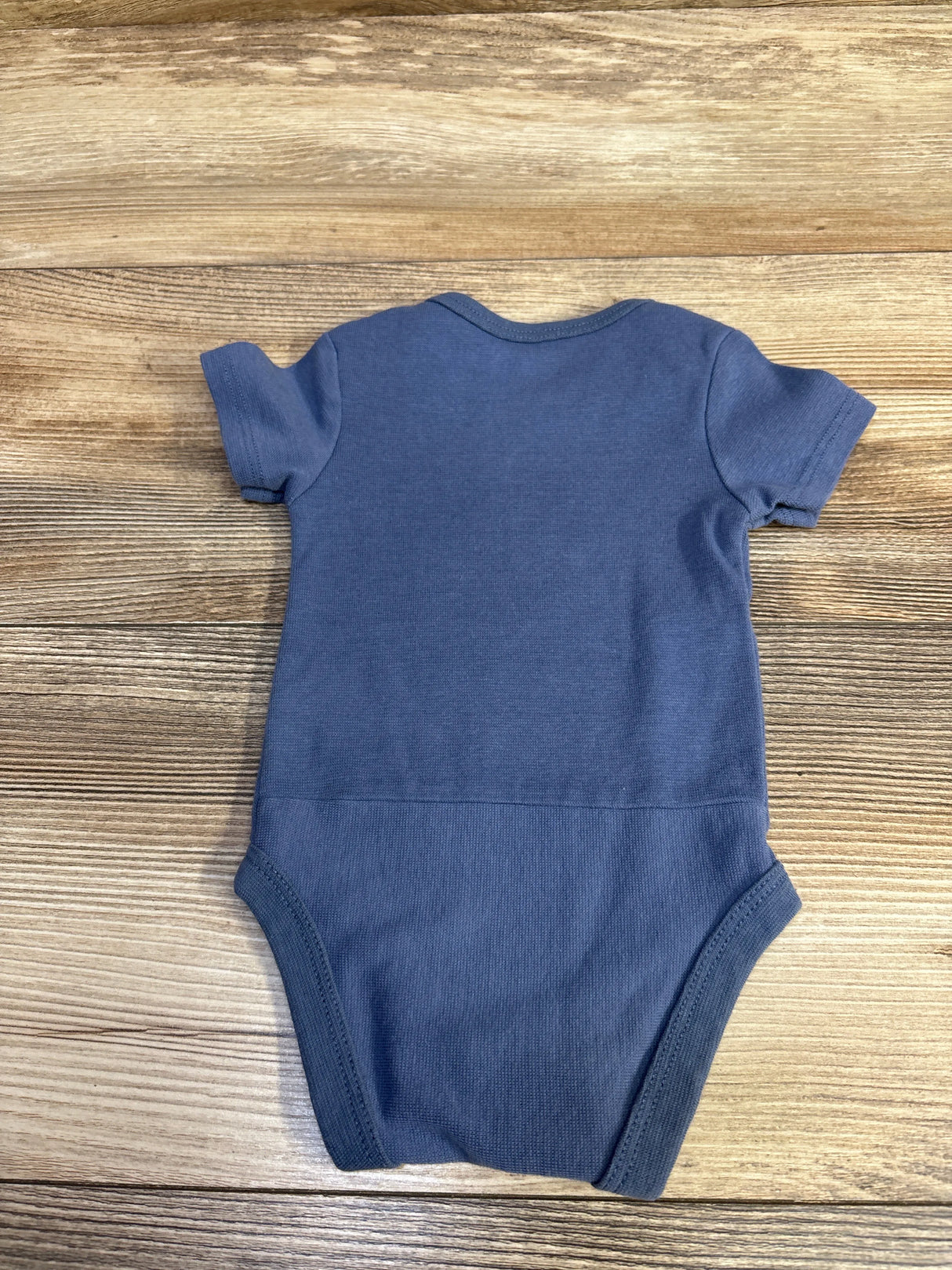 Back view of Hanes blue infant bodysuit showing short sleeves and ribbed leg openings on wood background