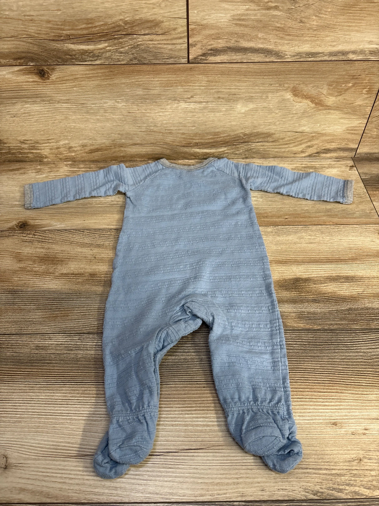 Back view of light blue Burt's Bees Baby organic footed sleeper showing ribbed texture and beige trim on wooden floor