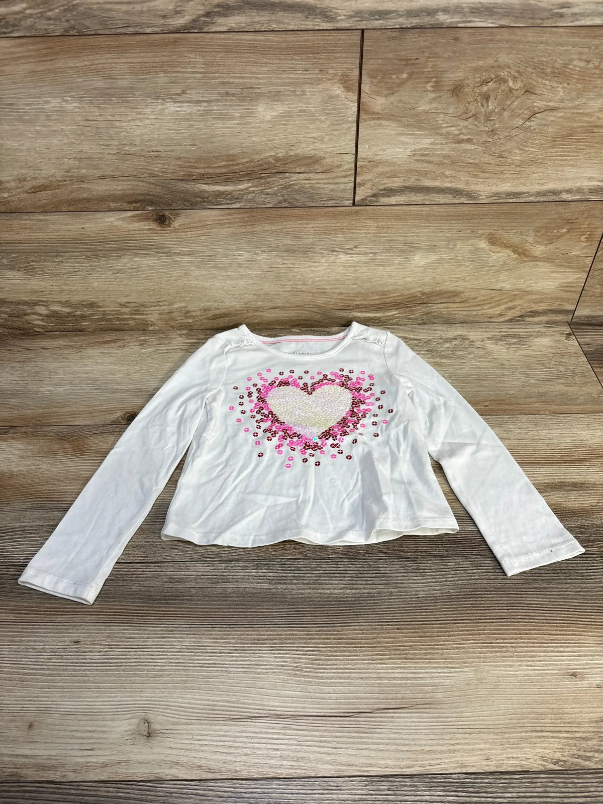 White long sleeve toddler shirt with pink sequin heart design on wood background