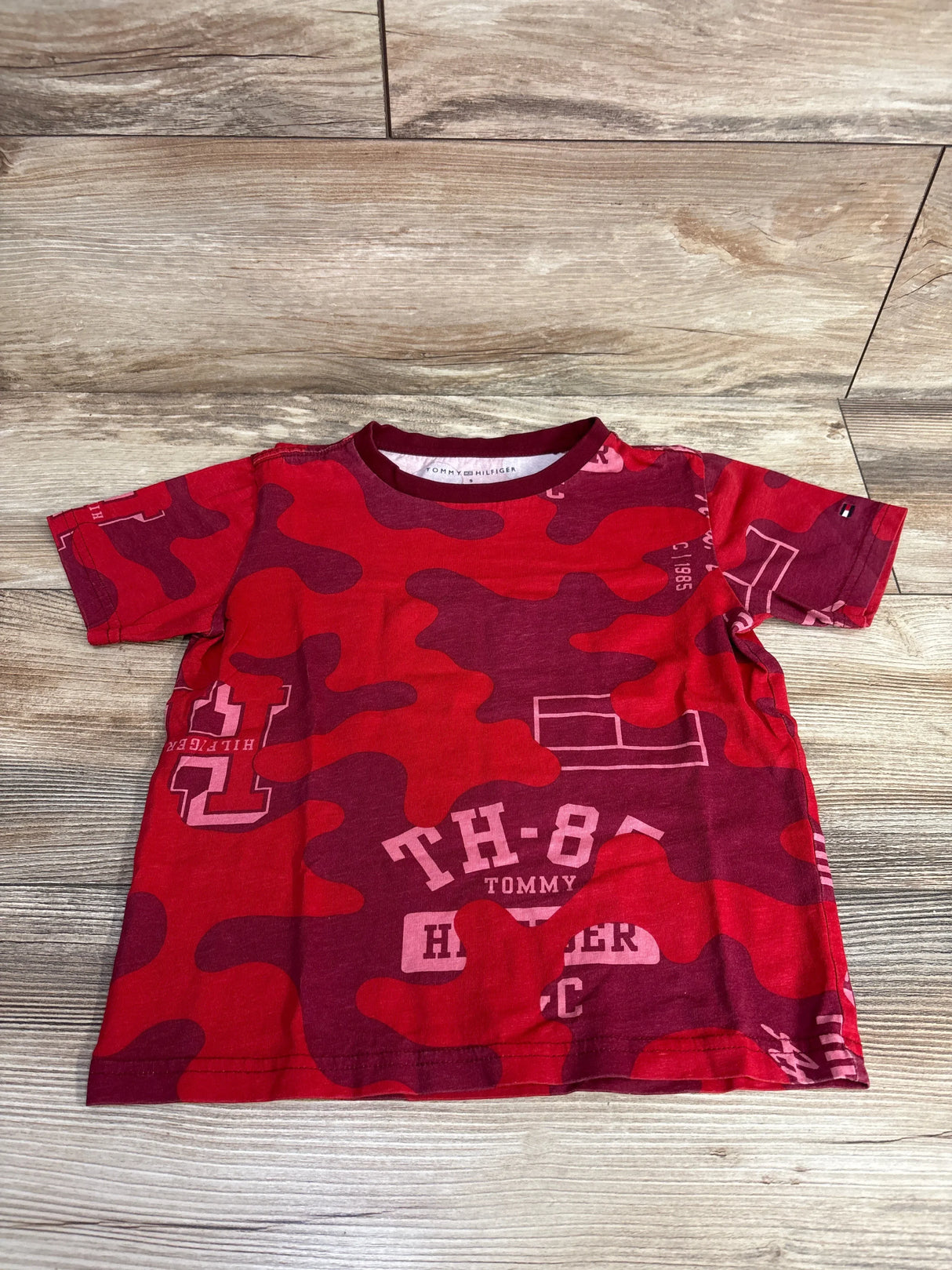 Red and burgundy camo toddler T-shirt with Tommy Hilfiger logo and text laid on wooden floor