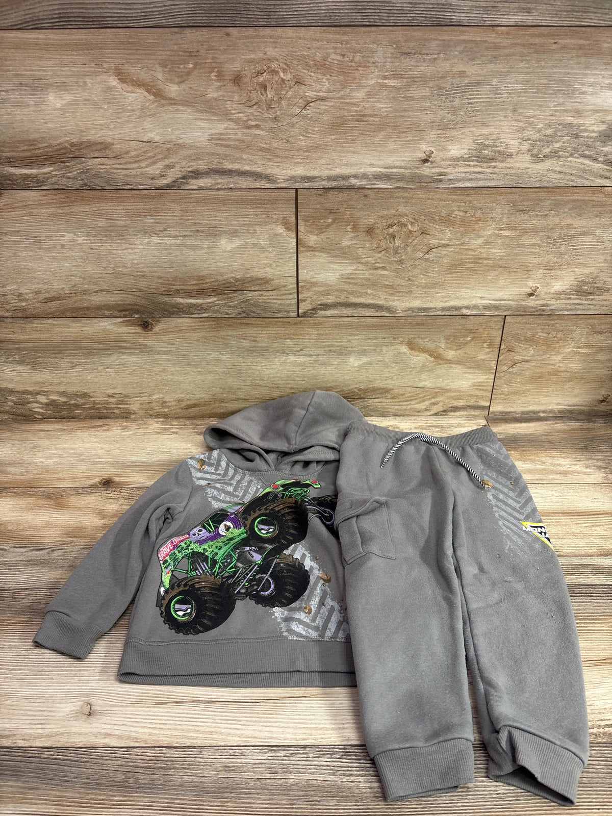 Top down view of grey Monster Jam pullover sweatshirt and joggers set featuring a monster truck graphic on wood flooring