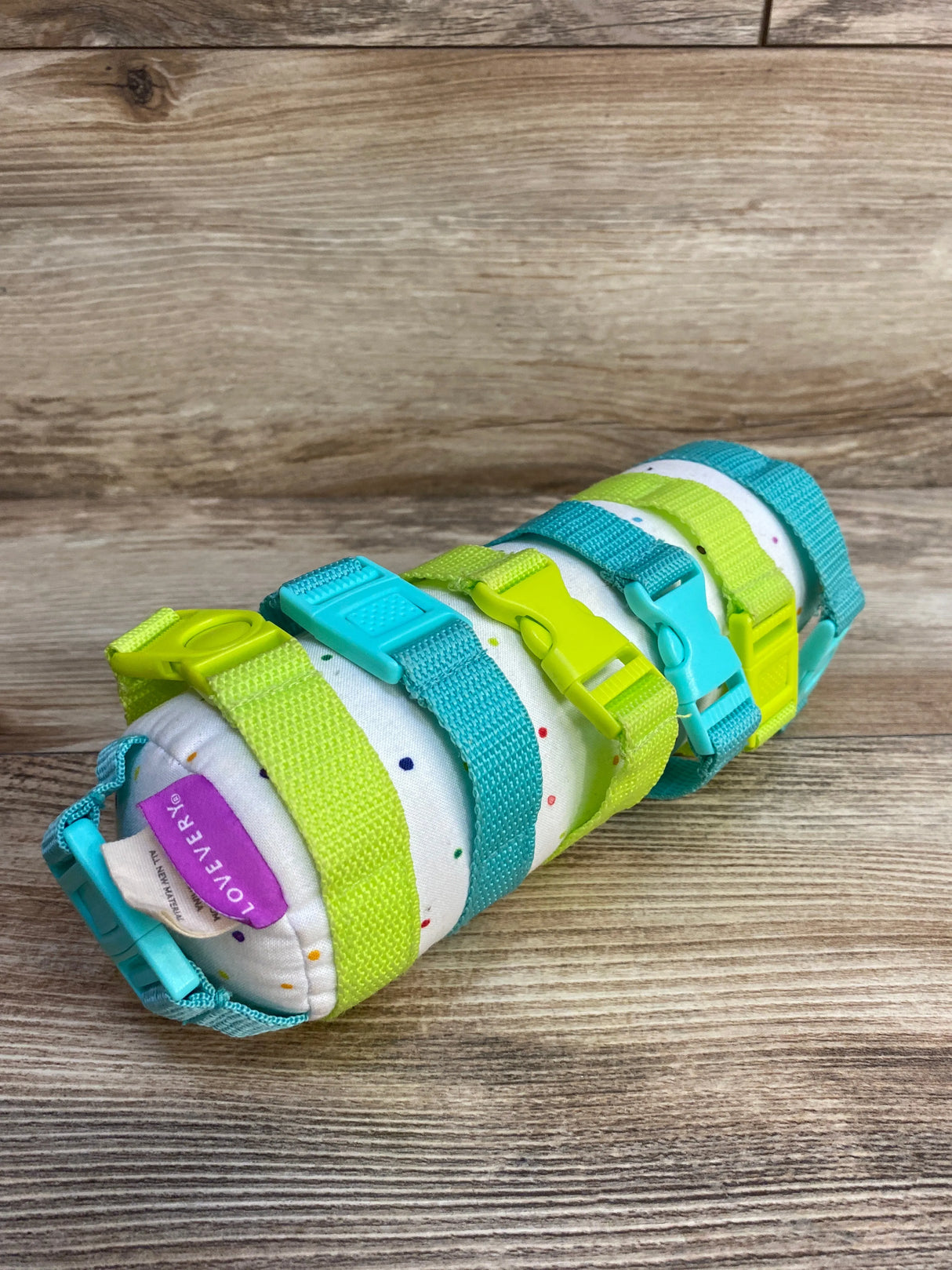 Rolled white fabric with multicolor dots secured by blue and green adjustable plastic straps on wooden surface