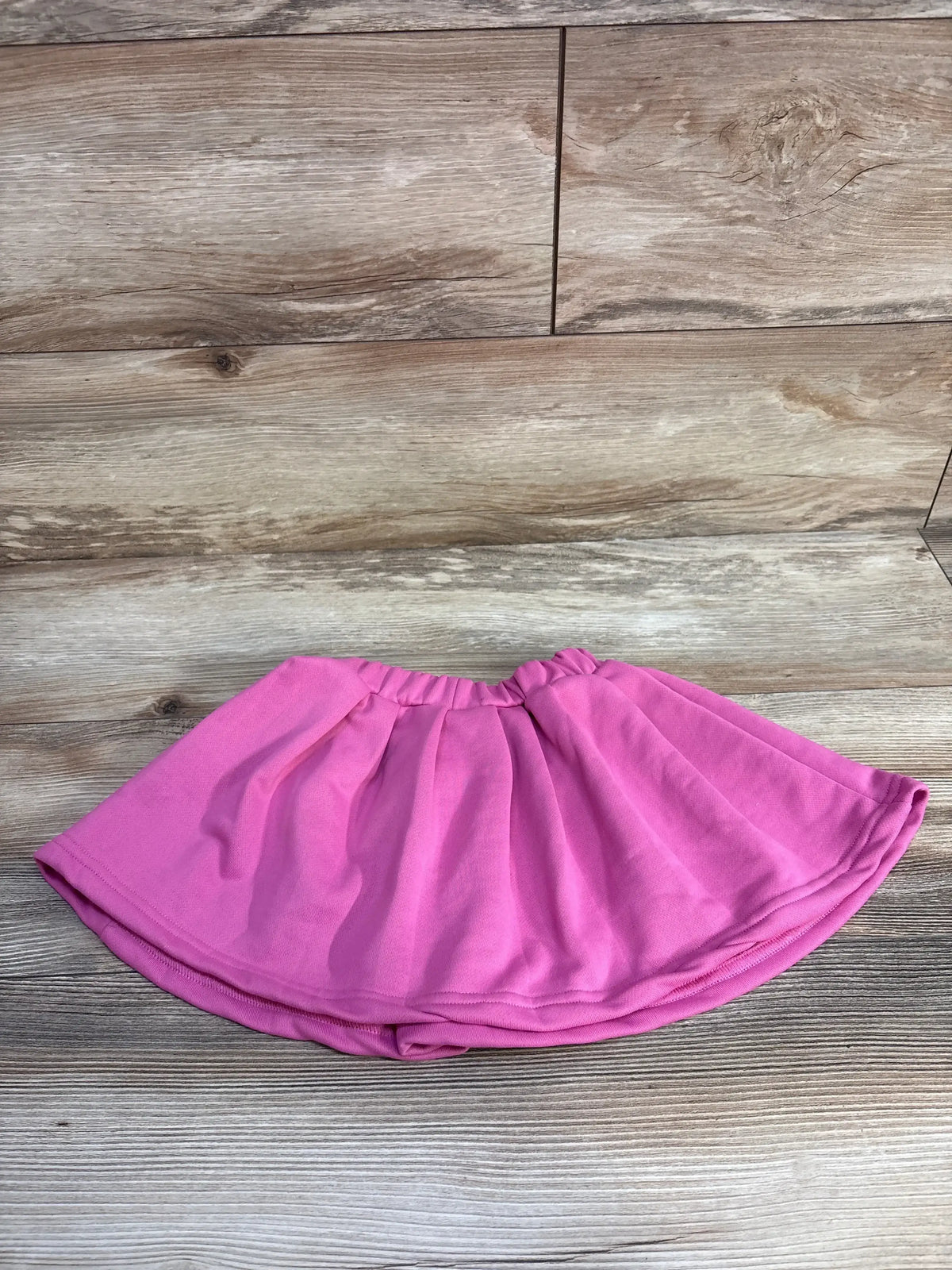 Flat lay of pink pull-on toddler skirt showing elastic waistband and flared A-line silhouette on wood background