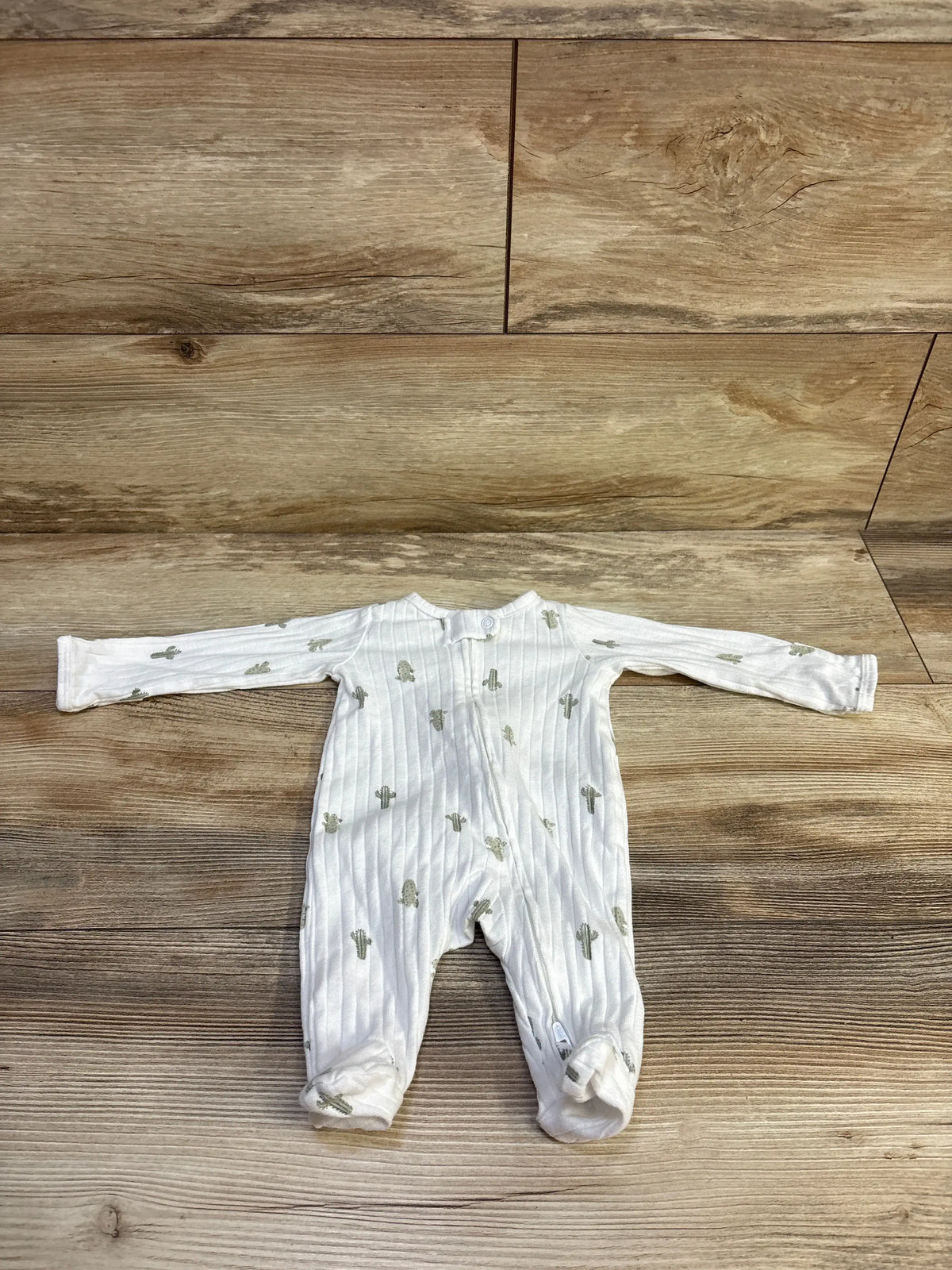 Flat lay of Child Of Mine ribbed newborn sleeper, white with green cactus print, footed with front snap, on wood background