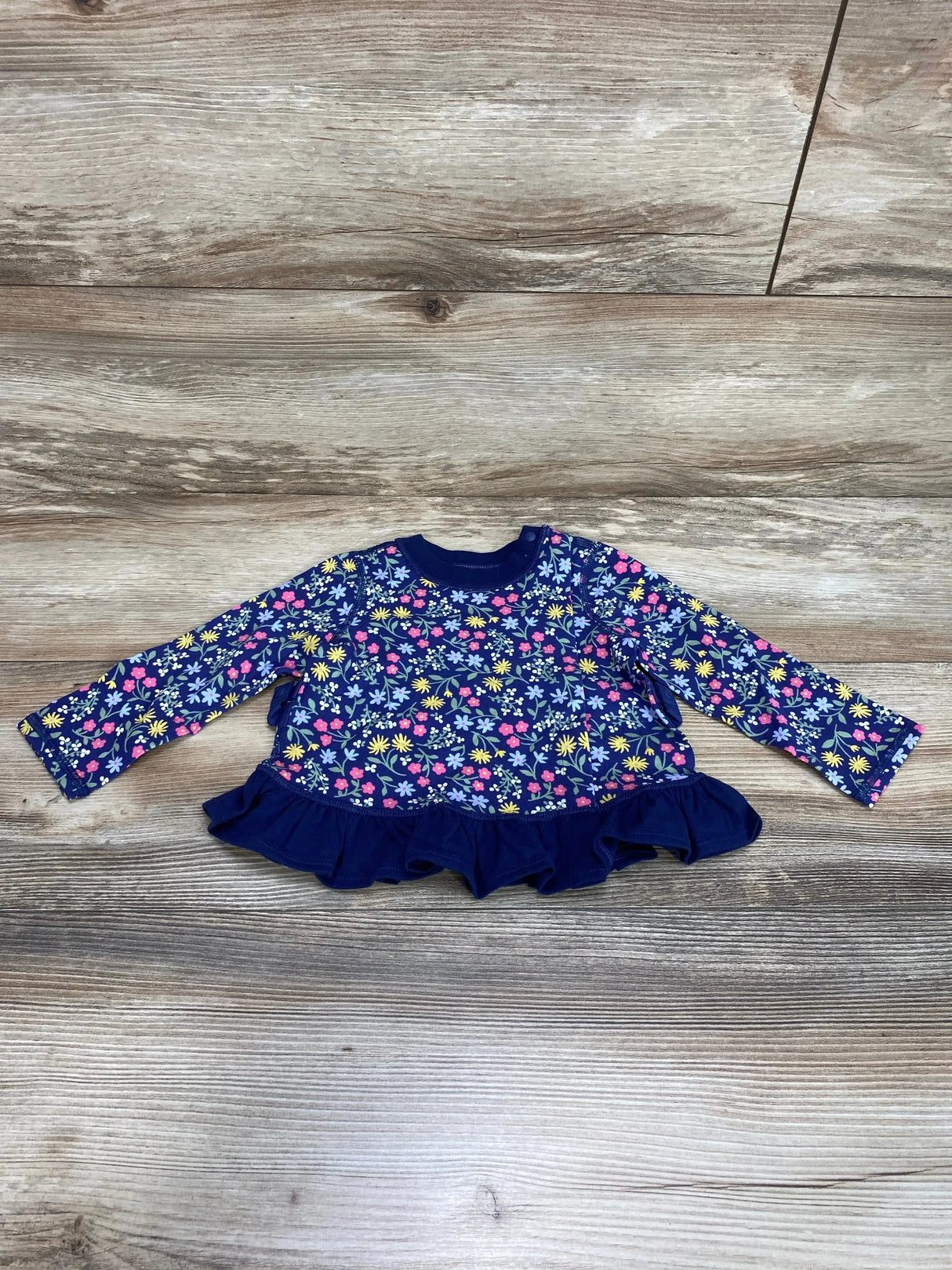 Flat lay of Cat & Jack baby peplum shirt showcasing floral print, long sleeves, and ruffled hem on wood surface