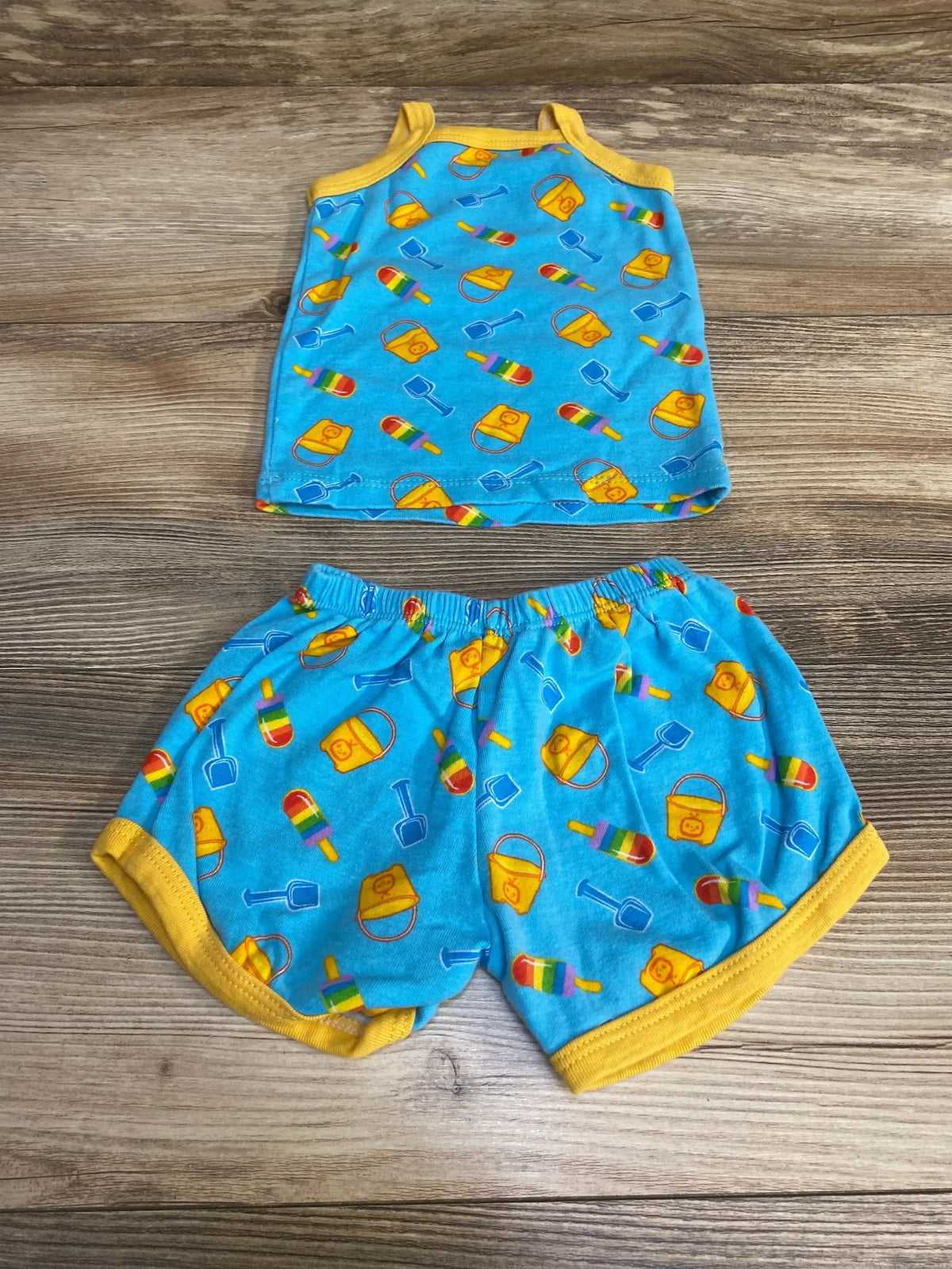 Flat lay of newborn blue Cocomelon top and shorts showing yellow trim, elastic waist and beach pail, shovel, popsicle print