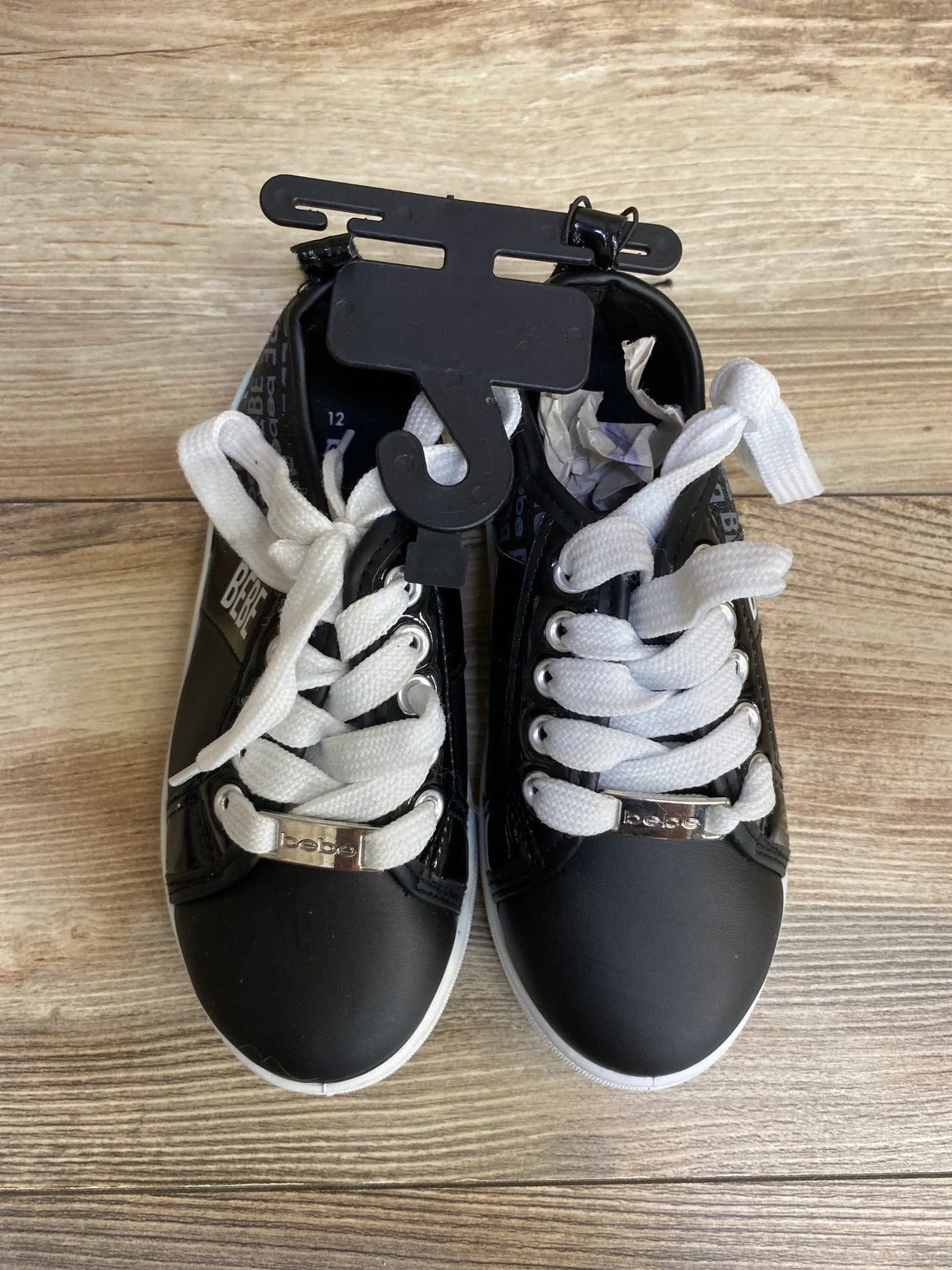Black Bebe sneakers with white laces on wooden floor, retail hanger attached