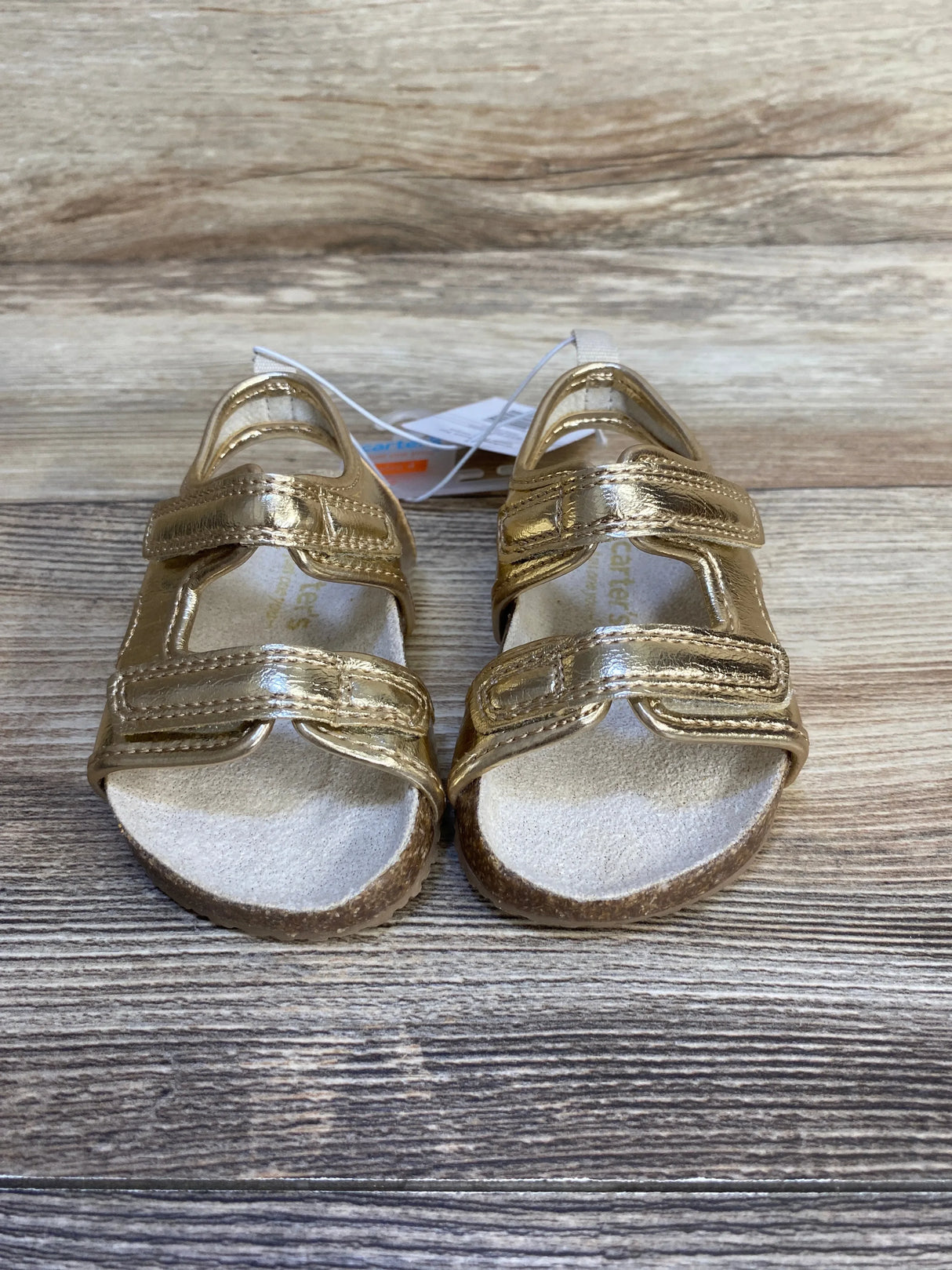 Front view of Just One You gold toddler sandals size 4C with two Velcro straps and cork soles on wood background