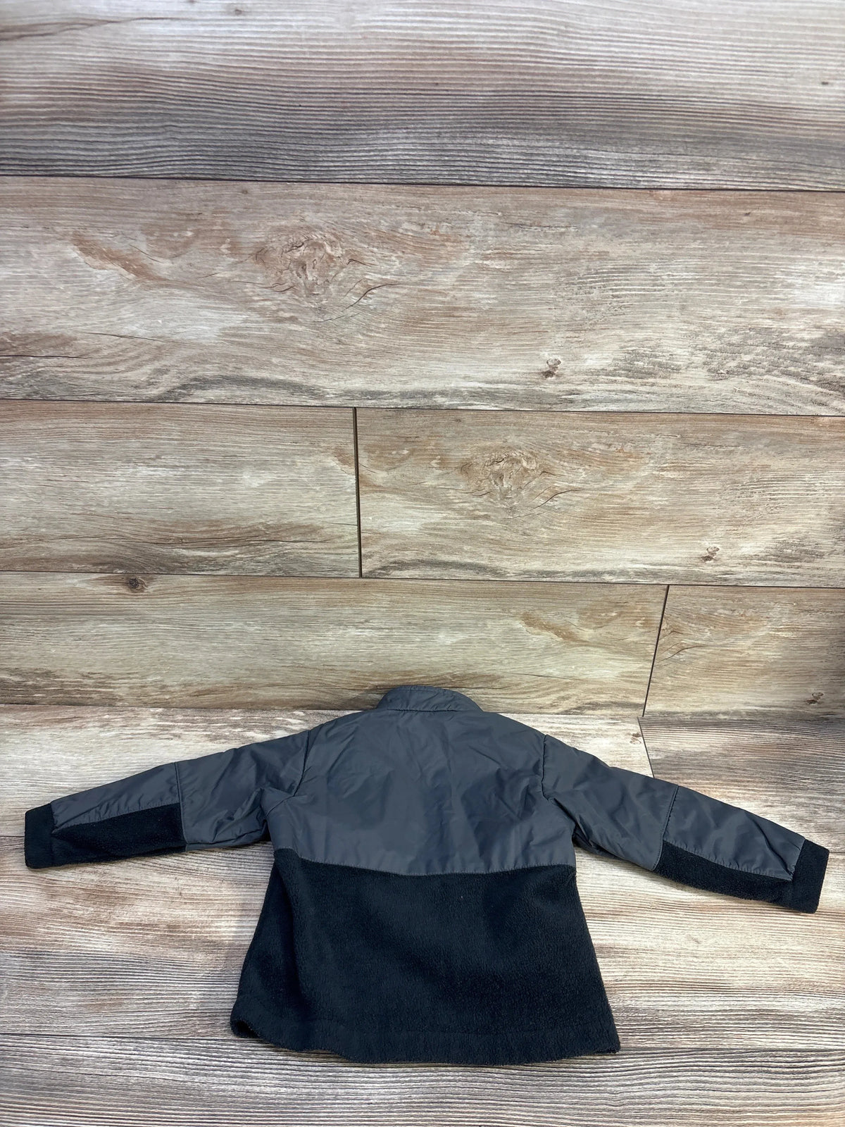 Back view of Columbia Steens Mt II toddler jacket showcasing grey nylon upper and black fleece lower with wood plank background