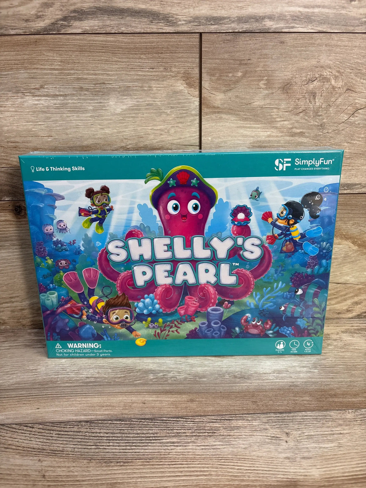 Front-facing box of Shelly’s Pearl board game showcasing large pink octopus artwork and game title with wooden floor background