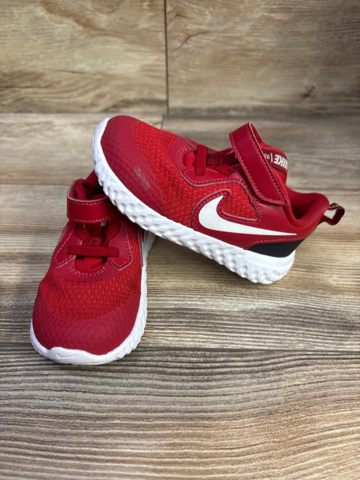 Angled view of red Nike Revolution 5 TDV sneakers with white swooshes, hook and loop straps, and textured soles