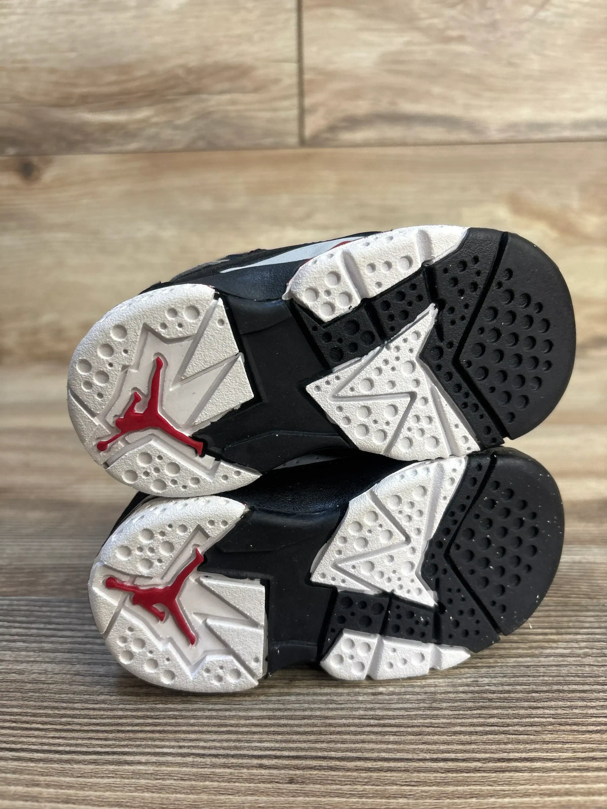 Kids' black and white athletic shoes with red Jumpman logo, rubber soles, wooden floor background