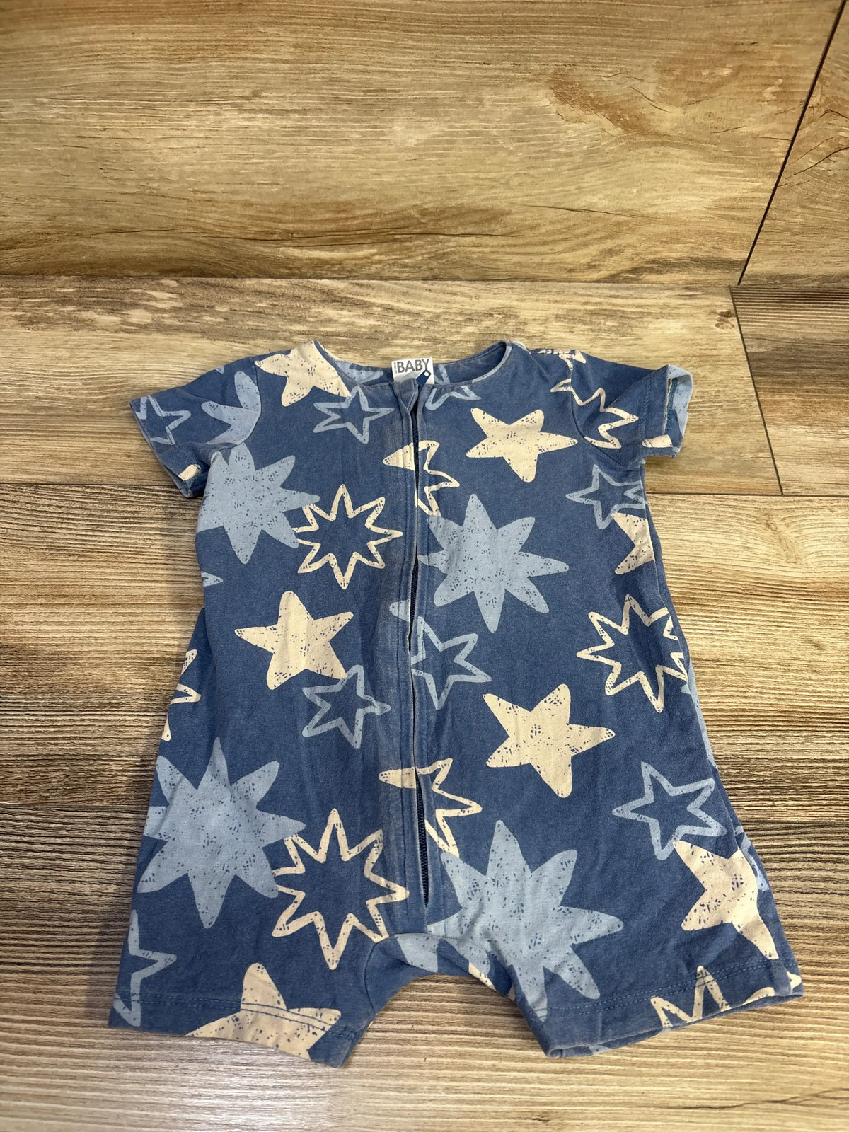 Front view of a blue baby short sleeve zip romper showcasing star pattern and front zipper on a wood floor