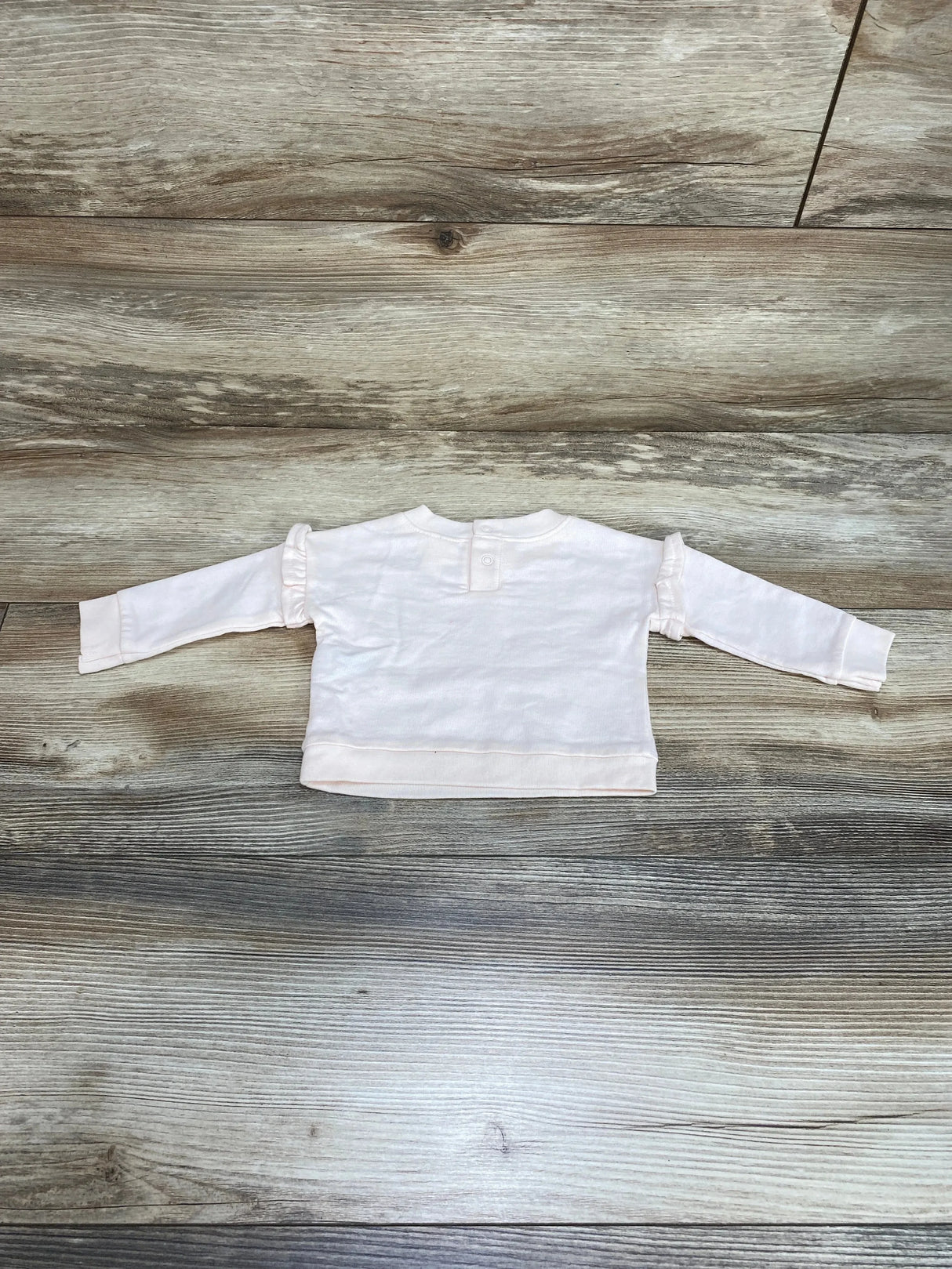 Back view of Cat & Jack newborn pink sweatshirt showing snap closure at neck and ruffle trim on sleeves on wood floor background