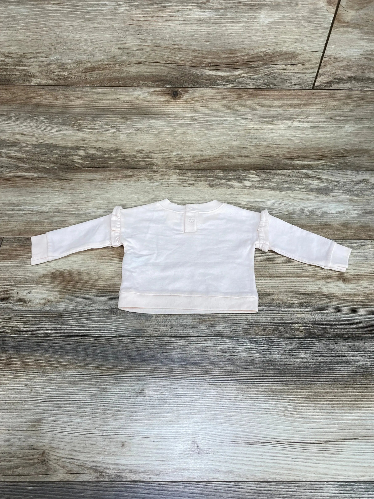 Back view of Cat & Jack newborn pink sweatshirt showing snap closure at neck and ruffle trim on sleeves on wood floor background