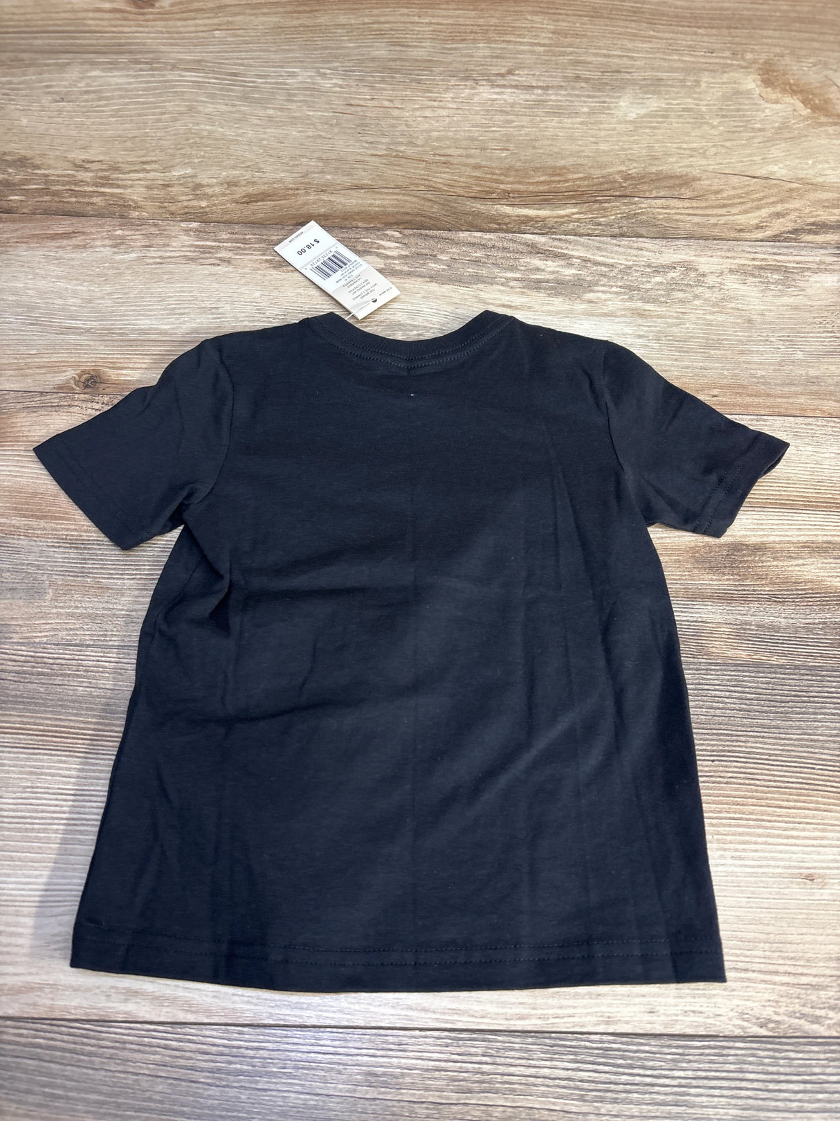 Black short-sleeve T-shirt with a price tag of $18.00 on wooden surface