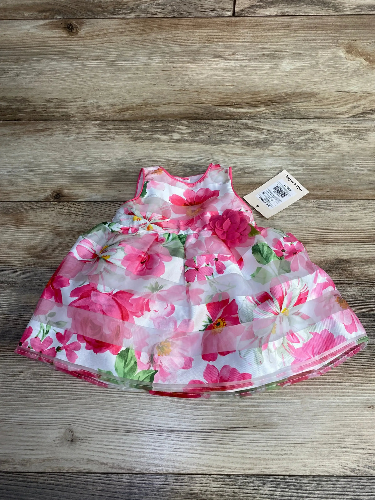 Top-down view of 2-piece baby floral dress and bloomers, white with pink flowers and layered organza skirt on wood