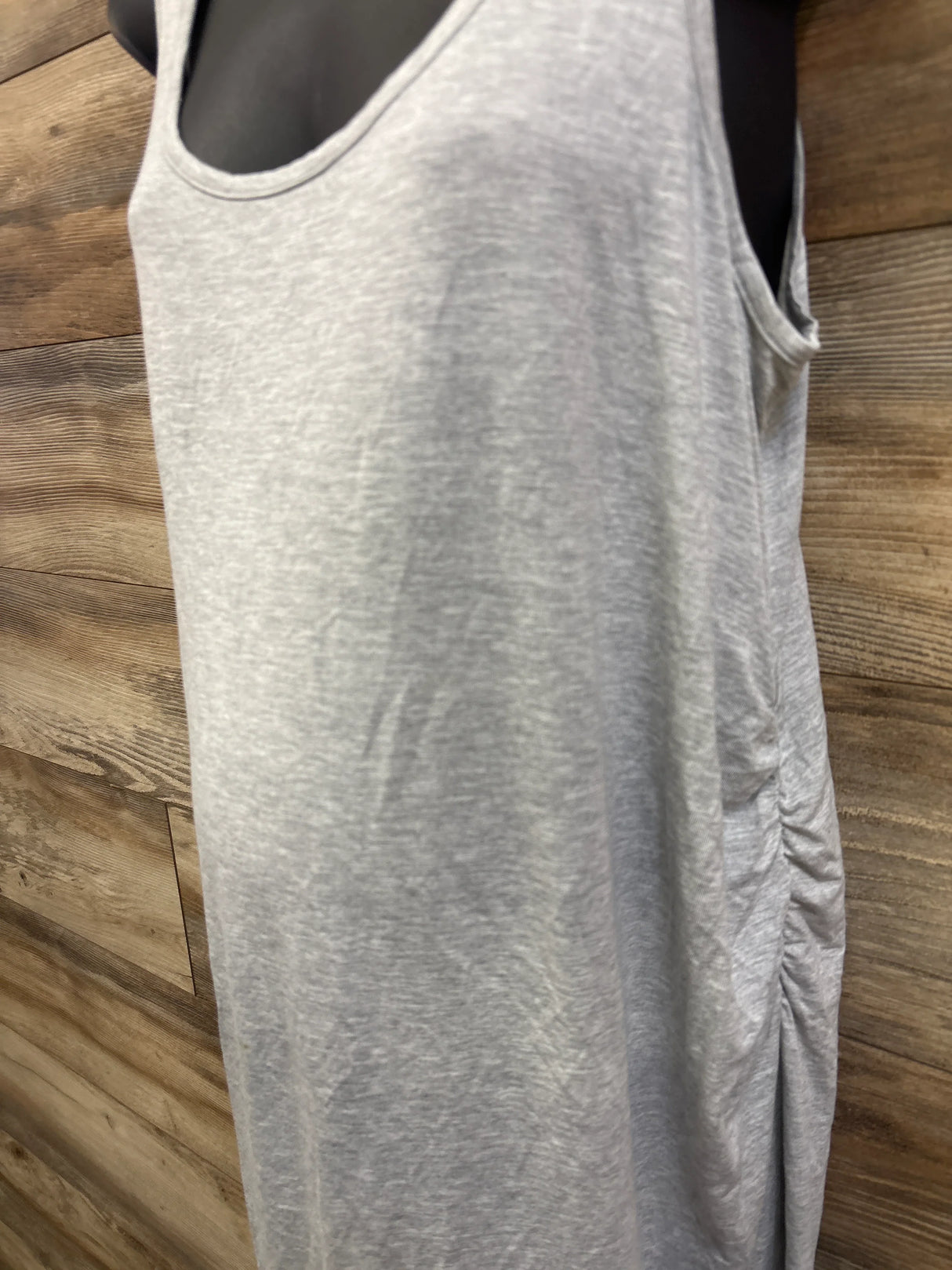 Close-up front view of grey maternity ruched tank dress showcasing side ruching on a mannequin against wood plank background