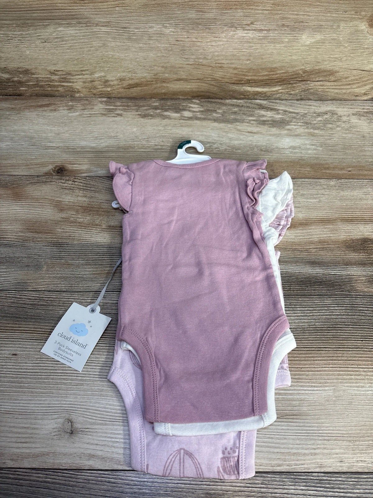Top view of Cloud Island three-pack pink sleeveless bodysuits in size 0-3 months showcasing layered designs on a wood surface