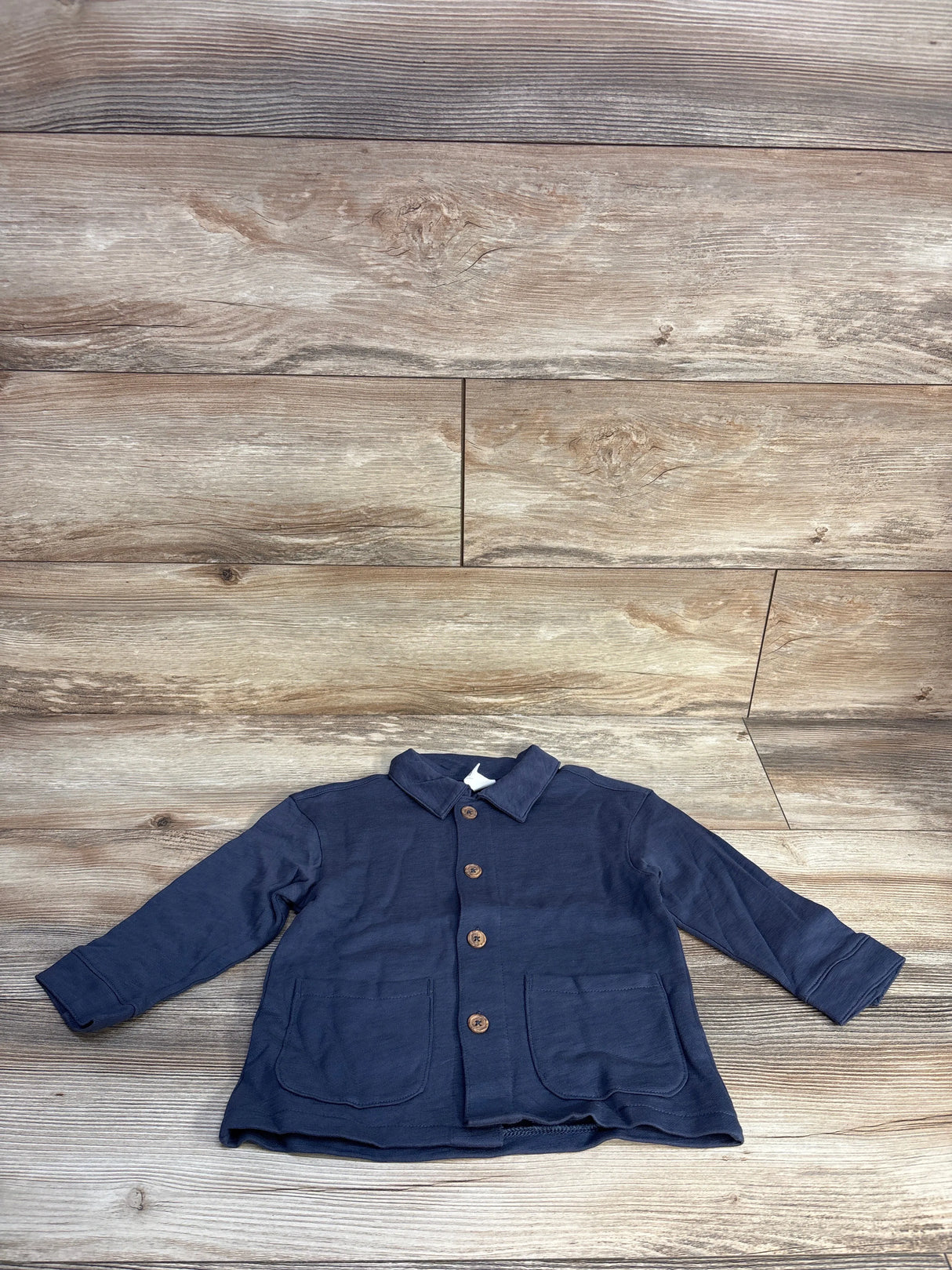 Navy blue toddler jacket with buttons and front pockets on wood background