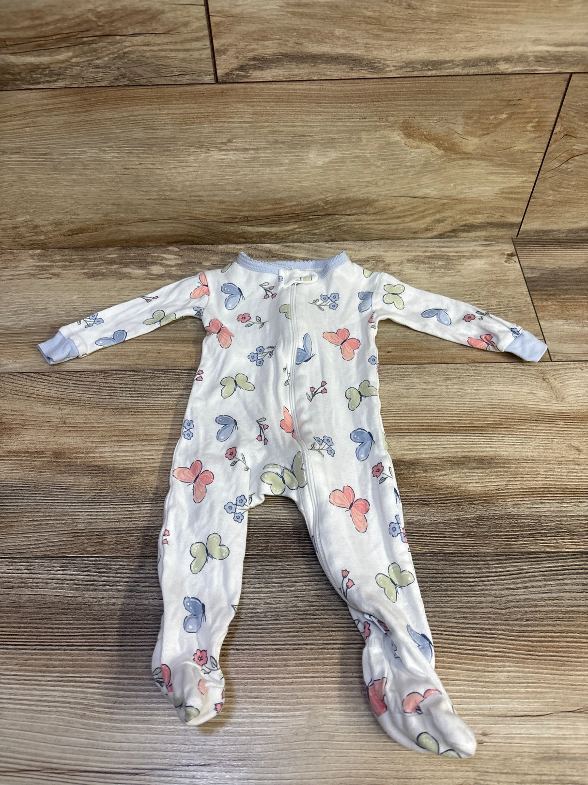 Flat lay of Gerber white footed sleeper size 0-3 months showcasing pastel butterfly print and zipper on wood background