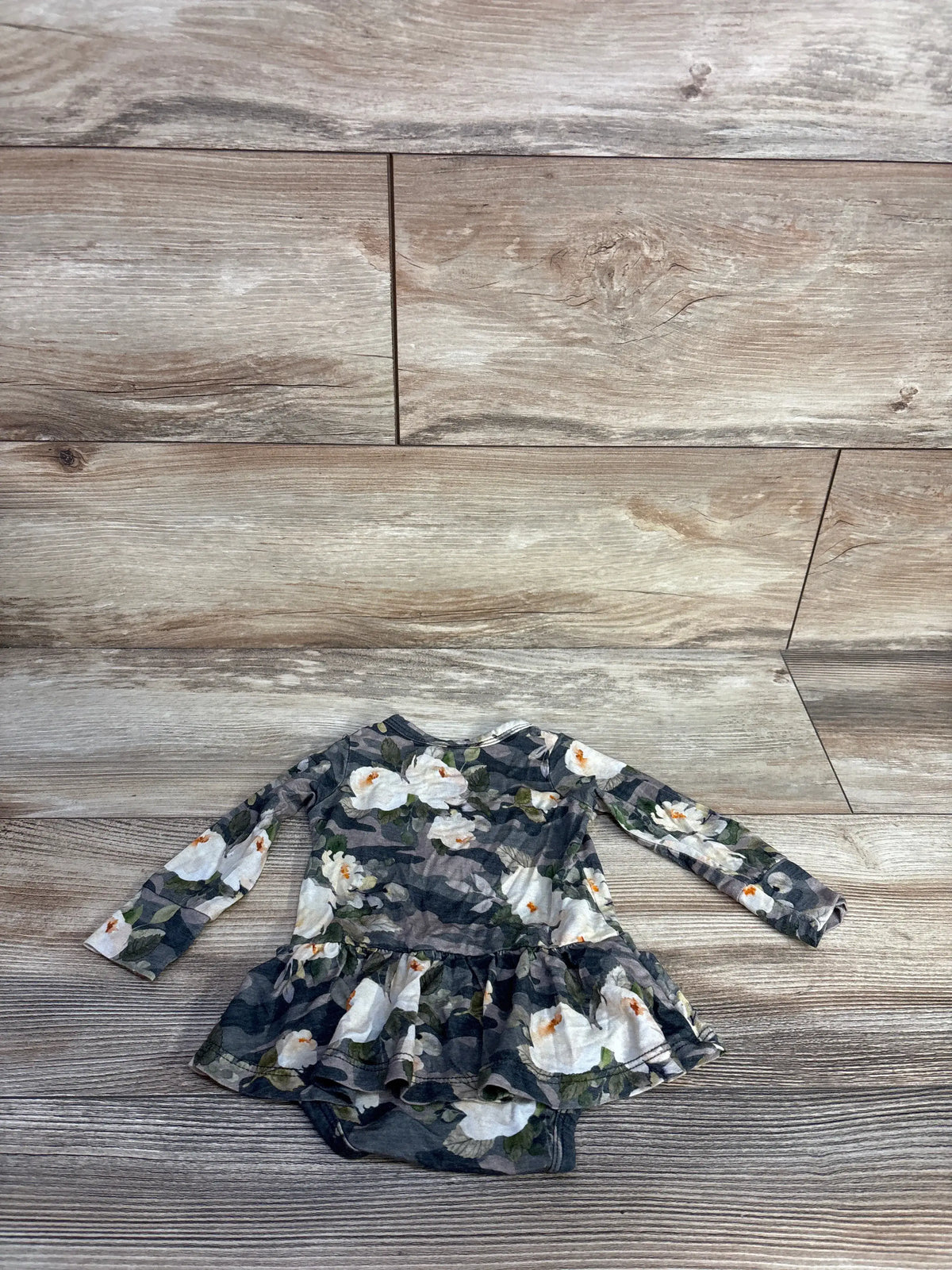 Front view of Gigi & Max bamboo tutu bodysuit showcasing its floral camo print and tutu skirt with a wood-look floor background