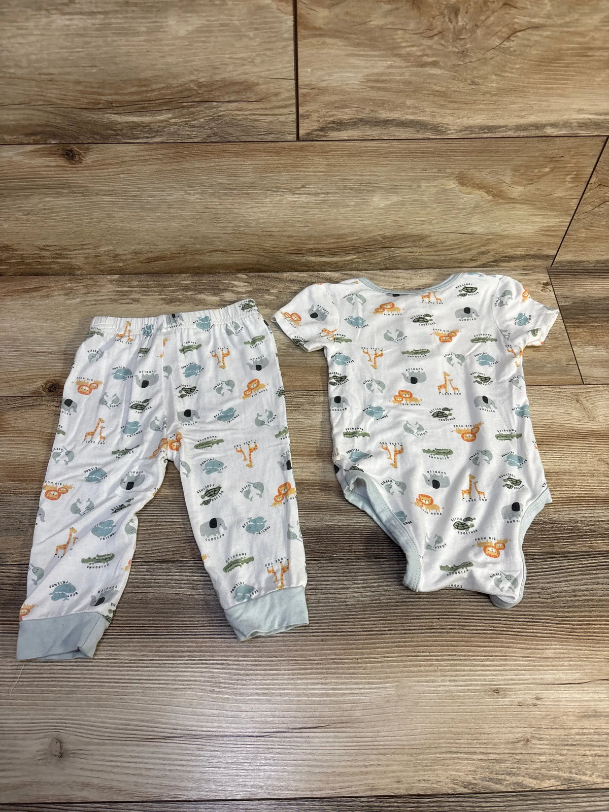 Top view of a white Milkberry bamboo animal bodysuit and pants set showcasing colorful animal print on a wood background
