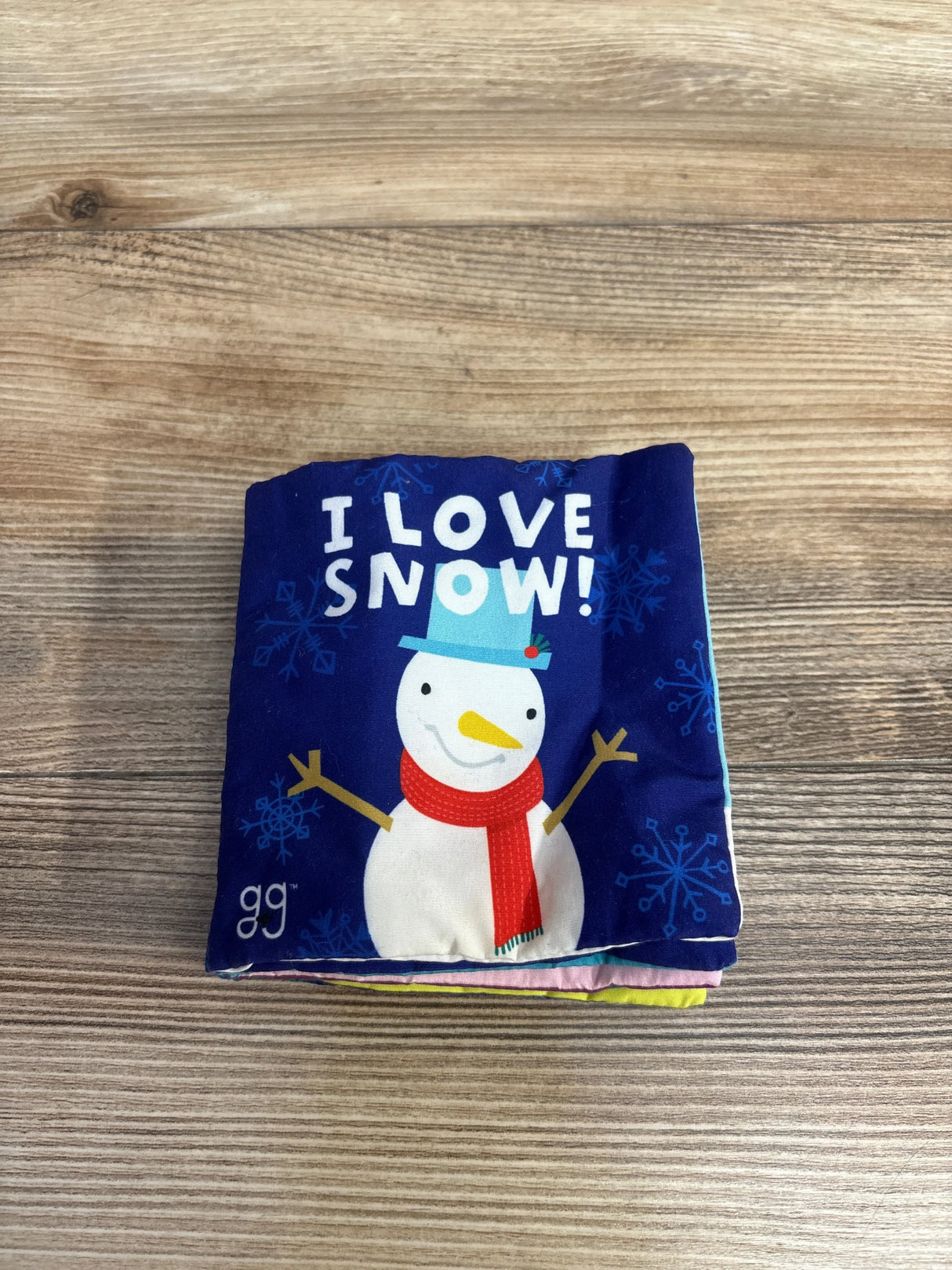 Soft baby cloth book with snowman and 'I Love Snow!' text on a wooden table