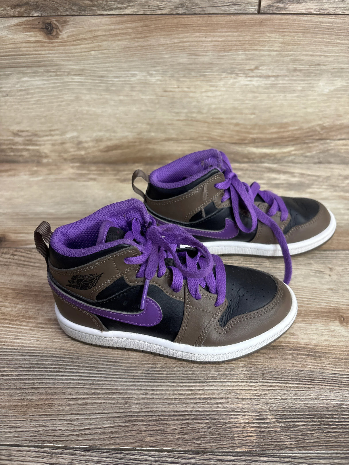 Pair of children's Air Jordan sneakers in brown, black, and purple with purple laces on wood floor