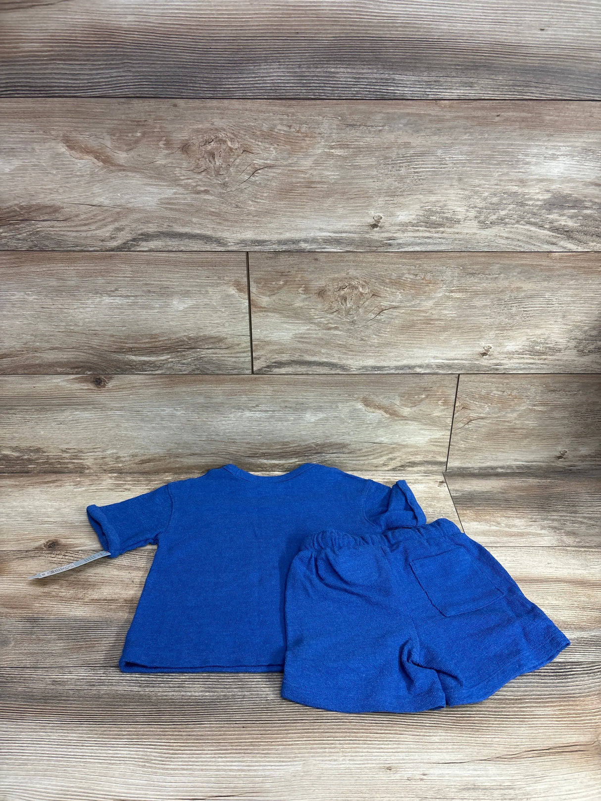 Flat-lay of blue toddler French terry shirt and matching shorts showing elastic waistband and back pocket on wood background