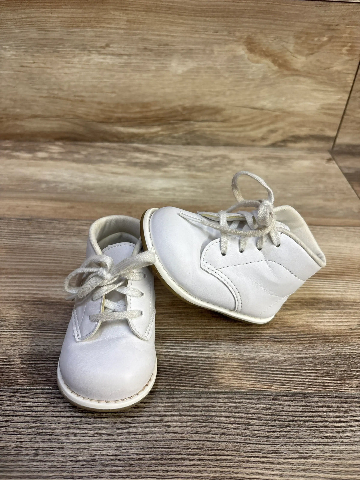 Front three quarter view of Teeny Toes First Walker baby shoes size 4C, white lace up with padded ankle and flexible sole on wooden surface