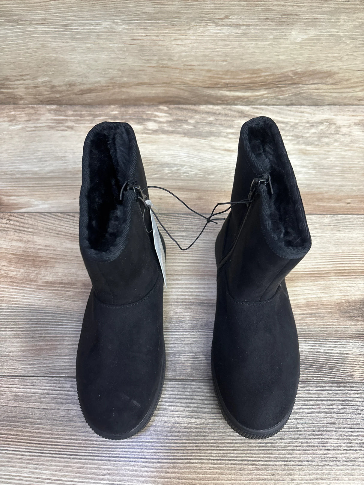 Front view of black children's fur lined winter boots with hangtag showcasing faux suede upper on wood plank floor