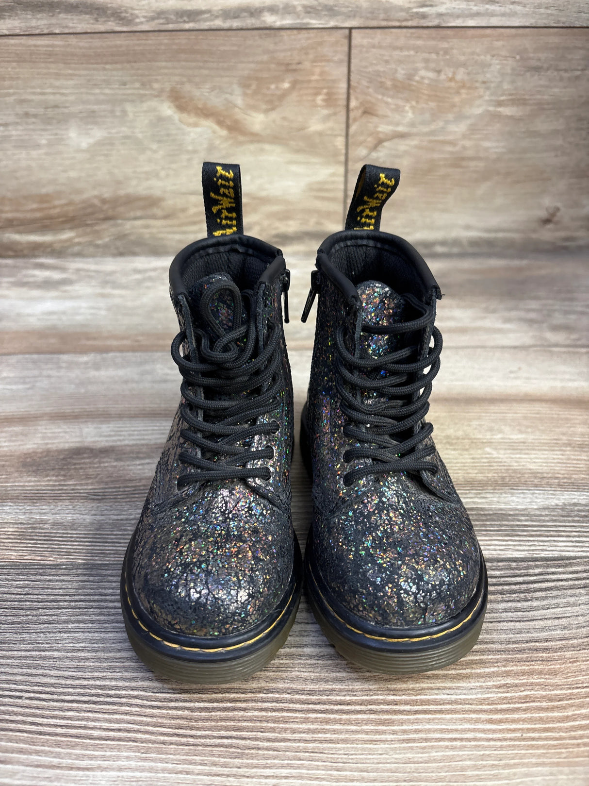 Front view of kids’ Dr. Martens 1460 Crinkle Metallic boots size 7C showing metallic glitter finish and yellow stitching on wood floor