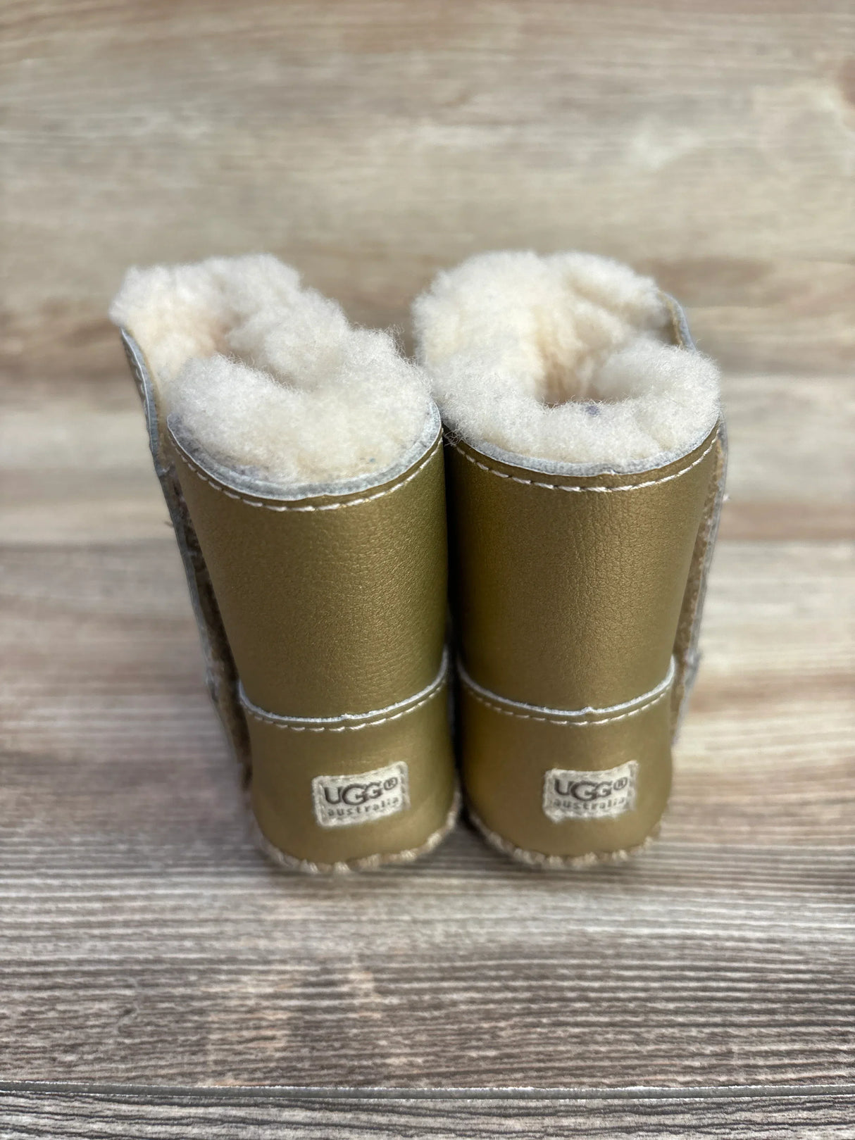 Pair of gold UGG Australia sheepskin boots with fluffy wool lining on wooden floor