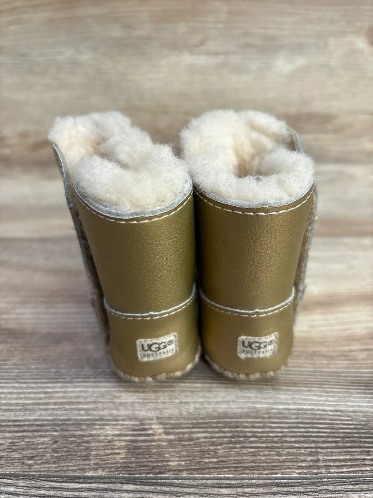 Pair of gold UGG Australia sheepskin boots with fluffy wool lining on wooden floor