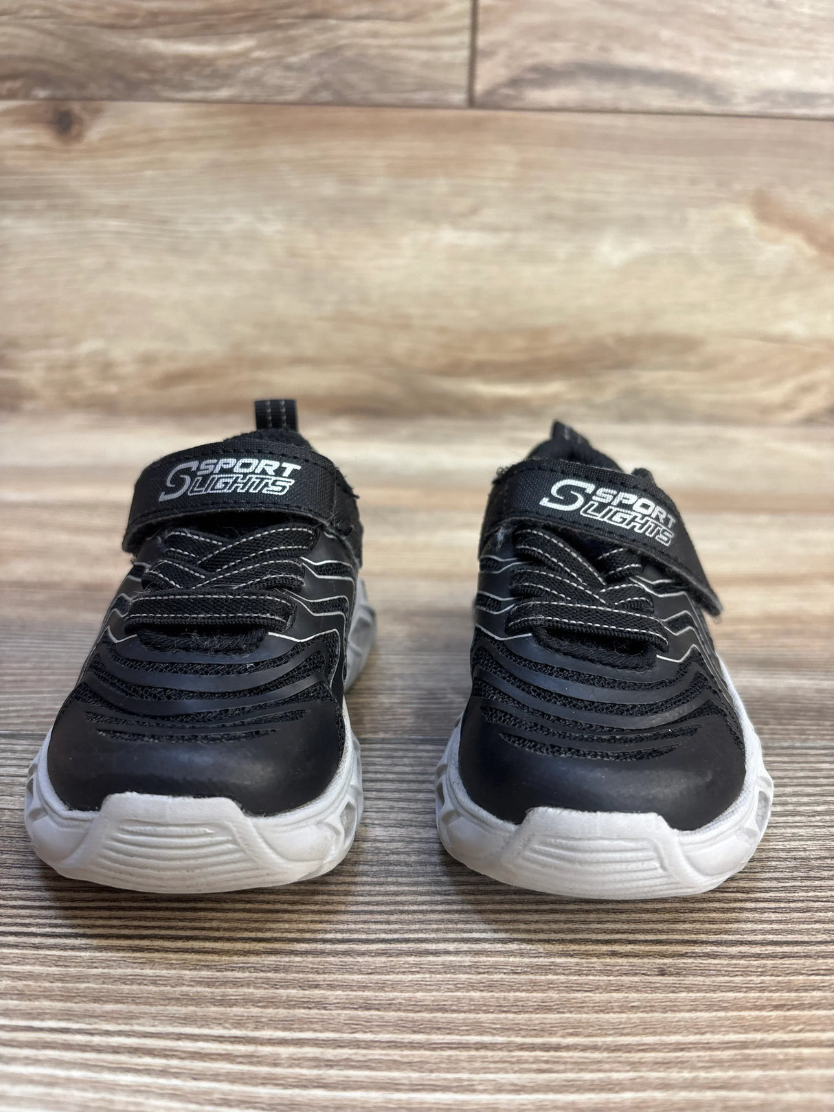 Black kids sport sneakers with white soles on wooden floor
