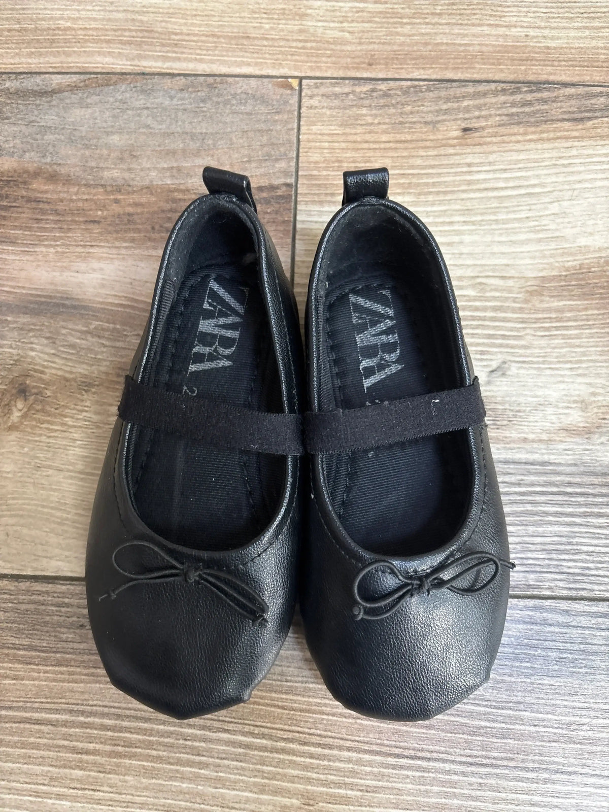 Black Zara ballet flats for girls with bow detail on wooden floor