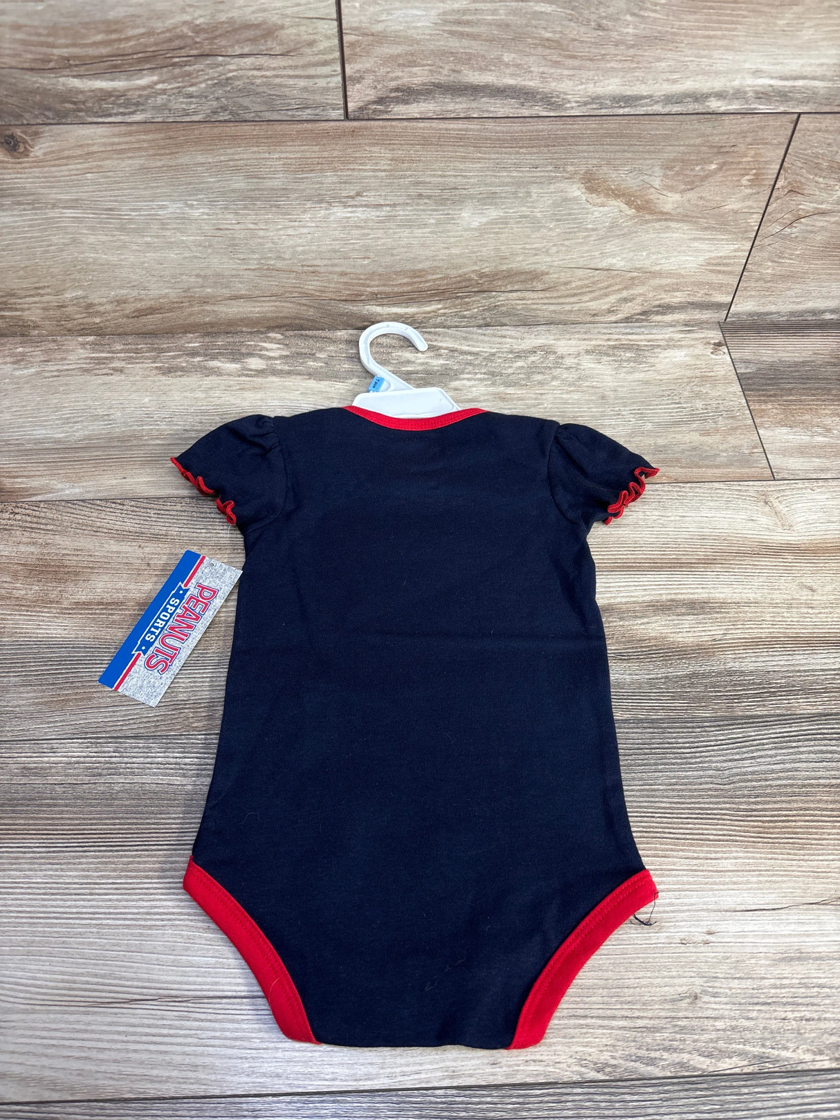 Navy blue baby onesie with red trim on sleeves, neckline, and leg openings on wooden floor