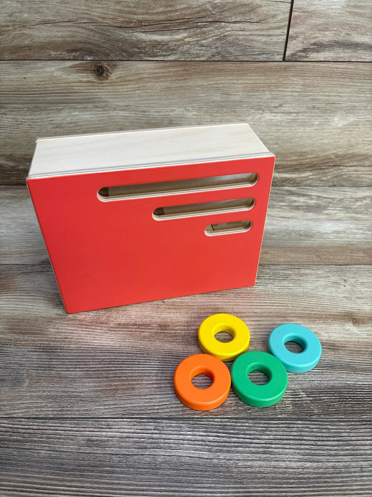 Angled front view of Lovevery Count & Slide Ring Chute showcasing three horizontal slots and four colorful wooden rings on a wood background