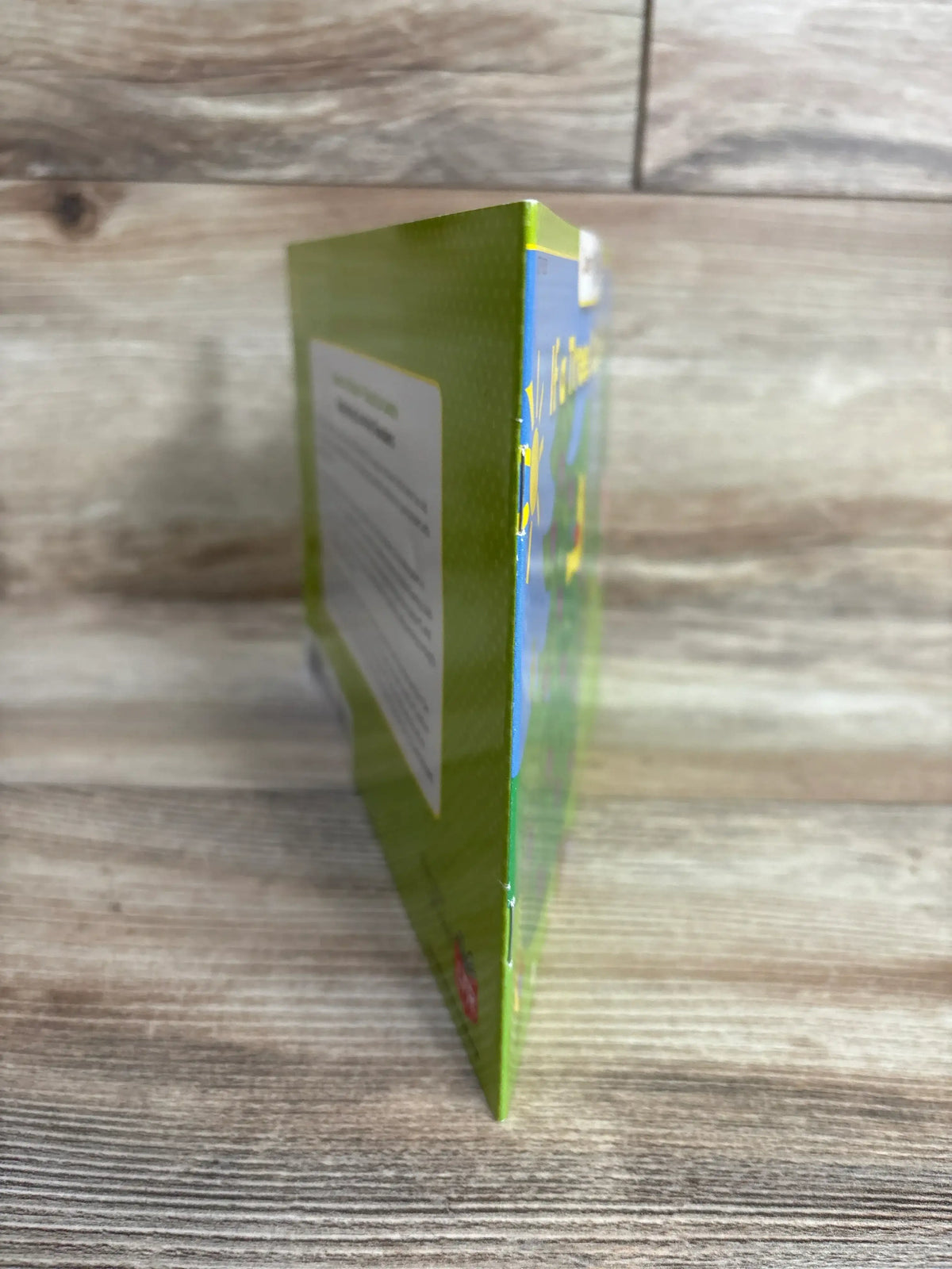Side view of If a Tree Could Talk paperback book showcasing green spine and back cover with blue sky front cover detail on wood plank floor