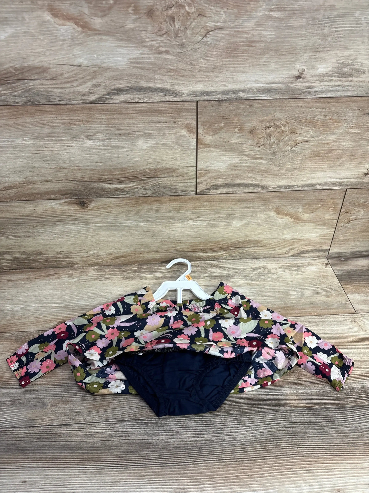 Top-down view of baby long-sleeve floral shirt and matching navy bottoms showcasing pink and olive floral print on navy with wood plank background