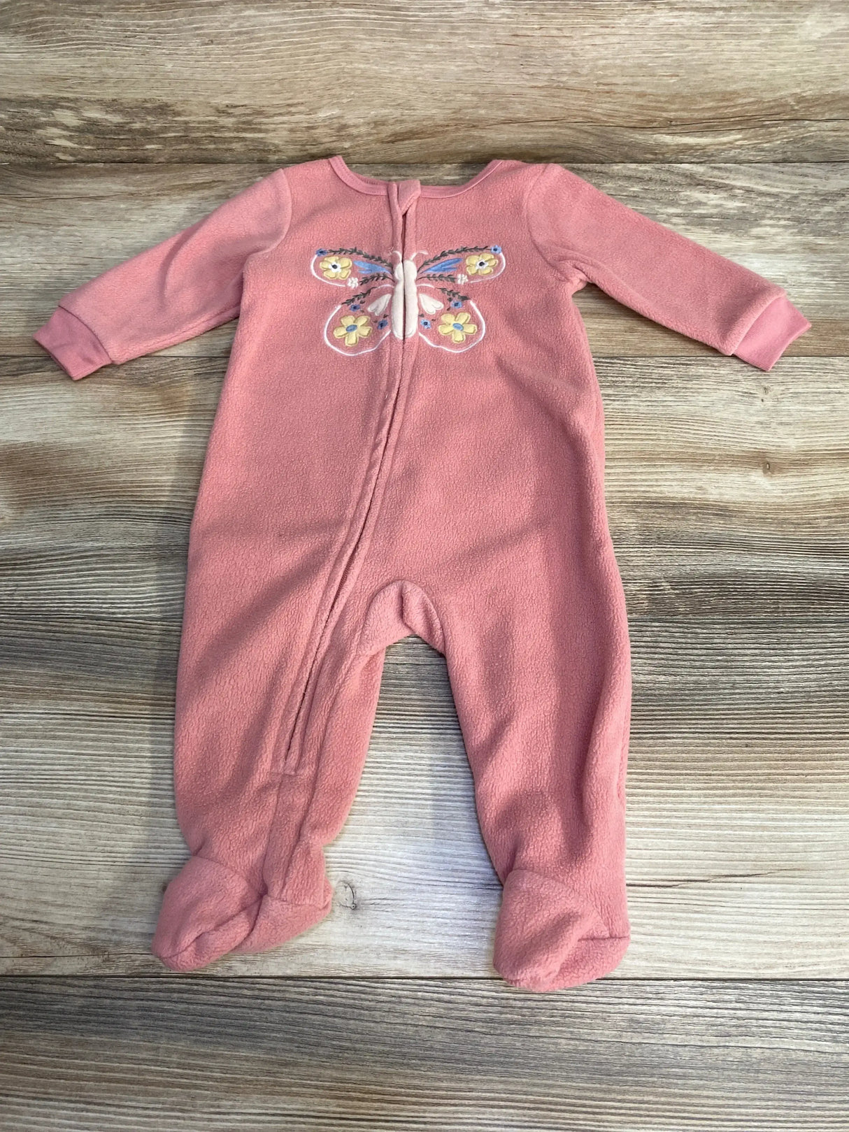 Top-down view of pink Kids Headquarters footed blanket sleeper showing embroidered butterfly on chest and front zipper on wood background