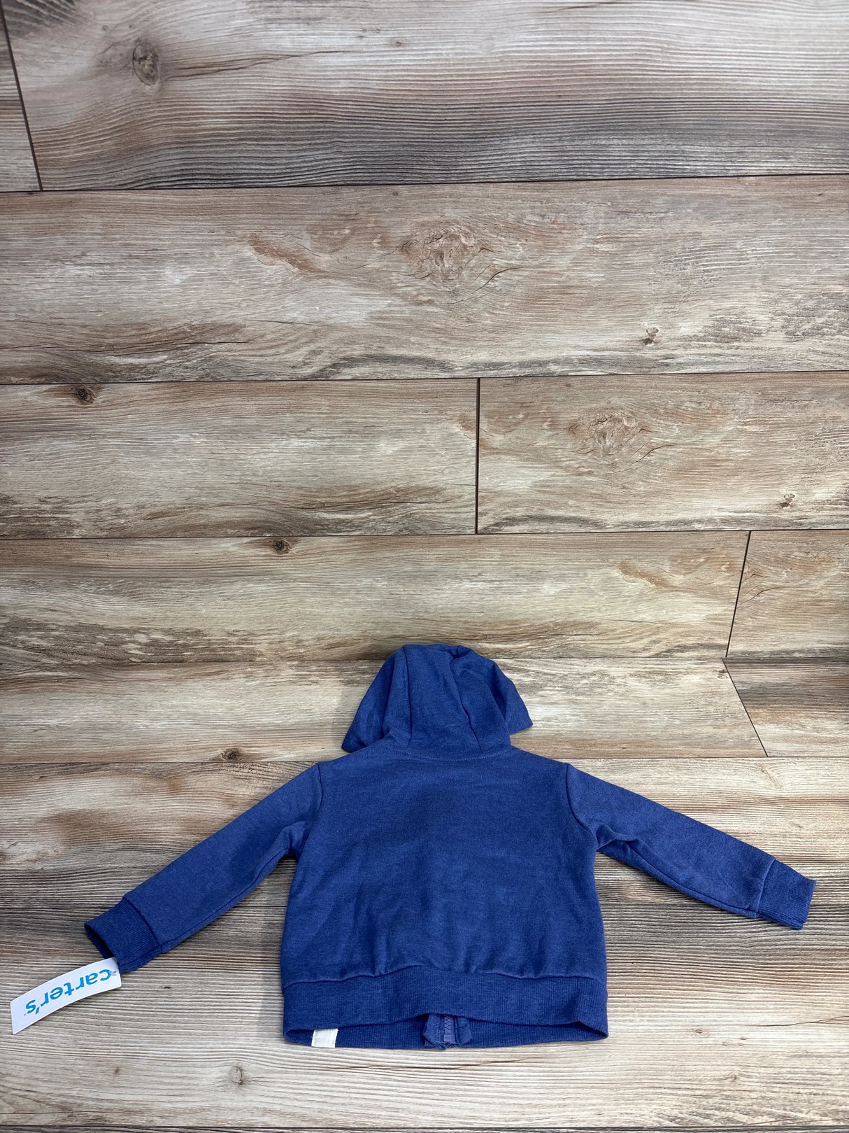 Back view of a blue toddler hoodie laid flat on wood floor, with Carter's brand tag attached