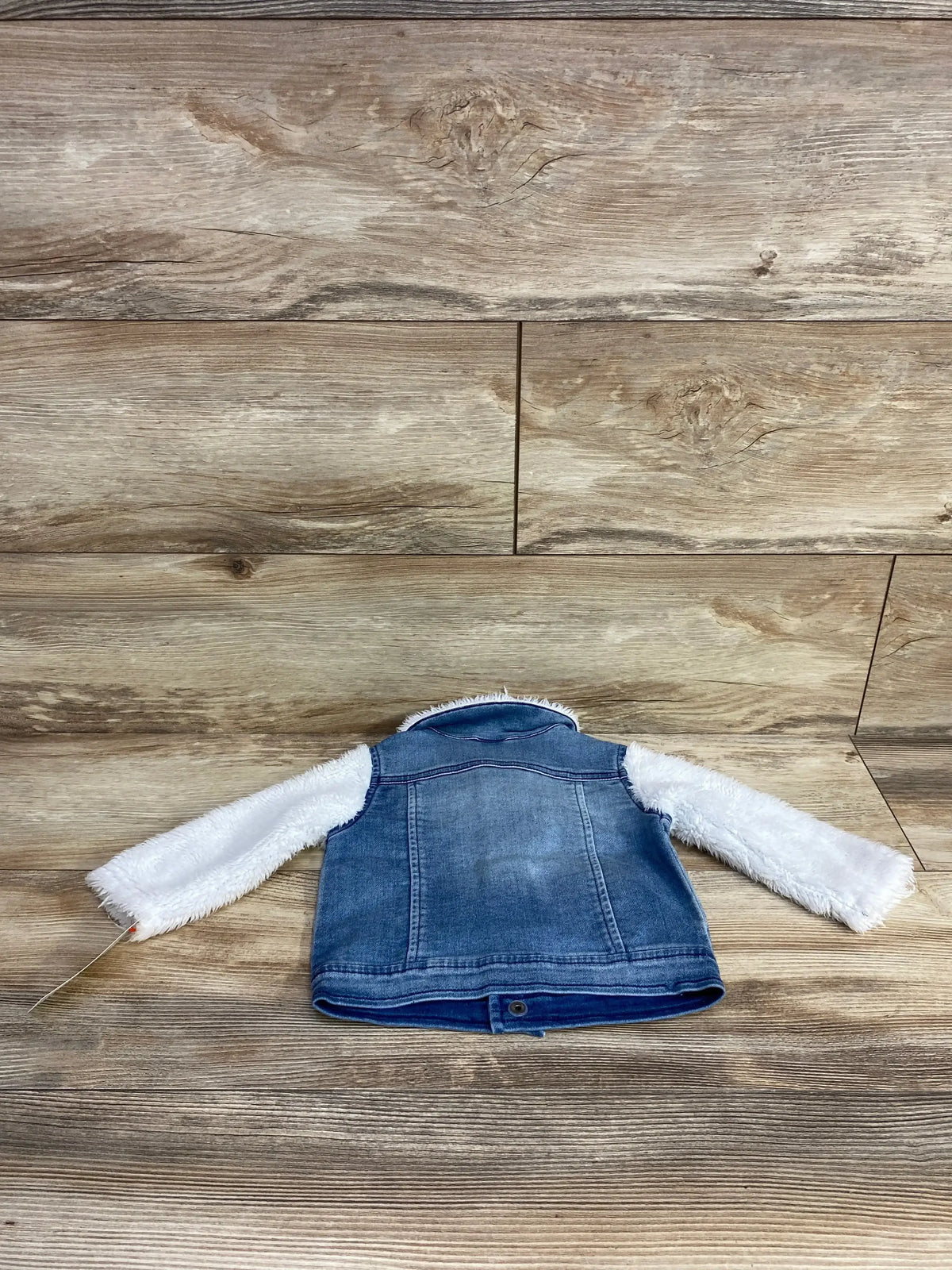 Back view of blue denim jacket with white fluffy sleeves on wooden floor