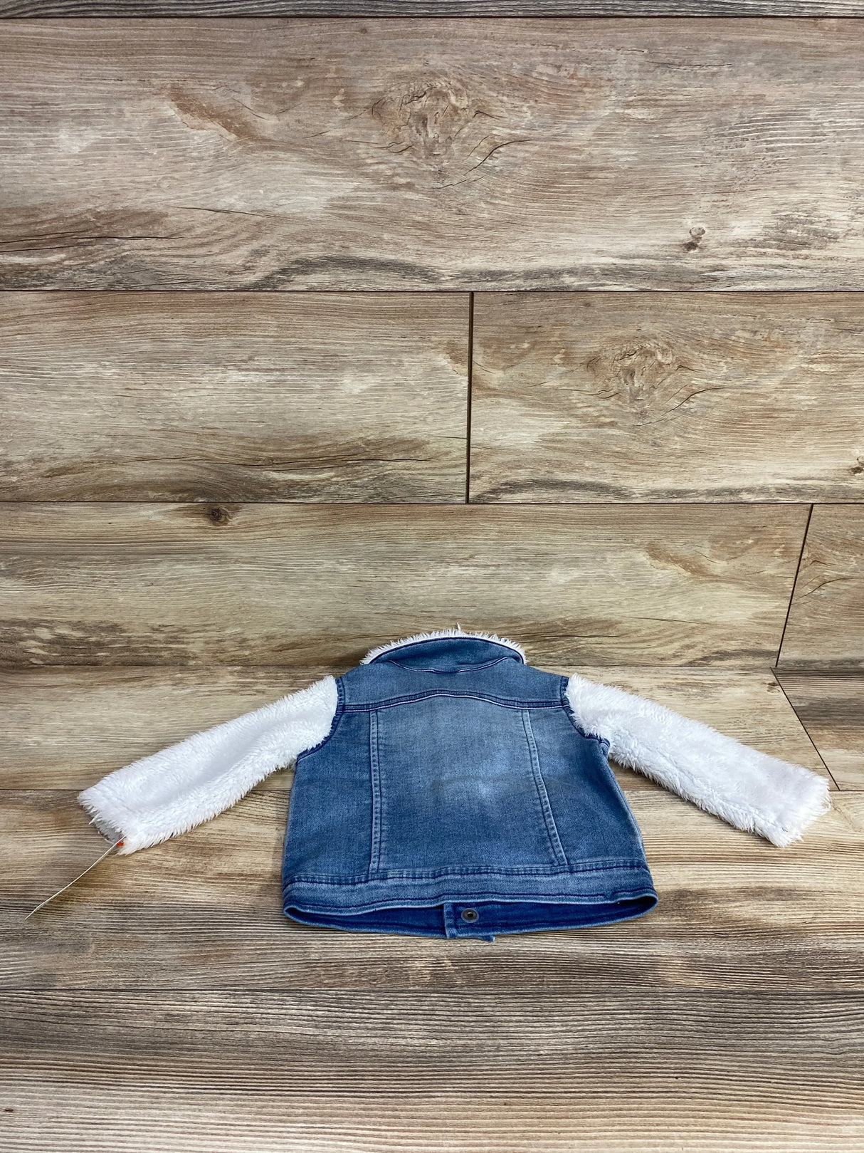 Back view of blue denim jacket with white fluffy sleeves on wooden floor