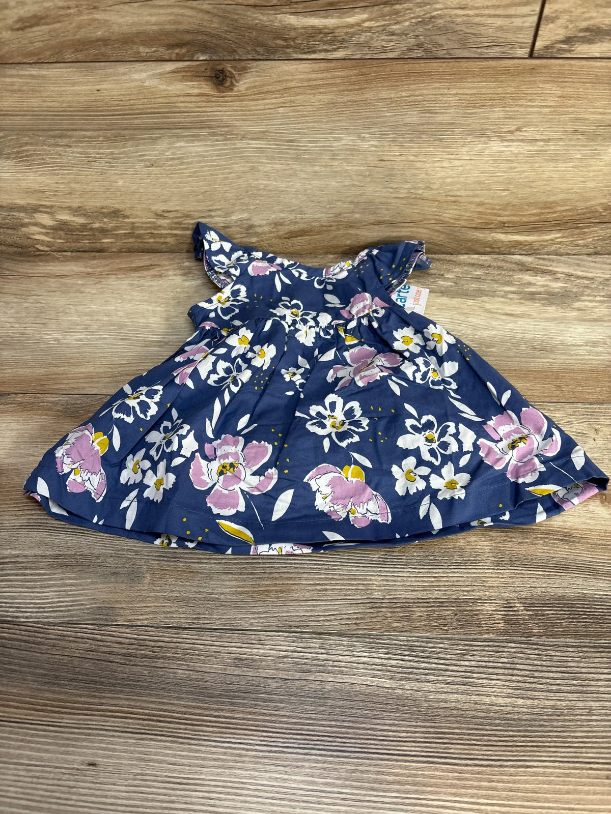 Front view of navy blue baby dress with pink and white floral print, flutter sleeves, and gathered waist on wood background