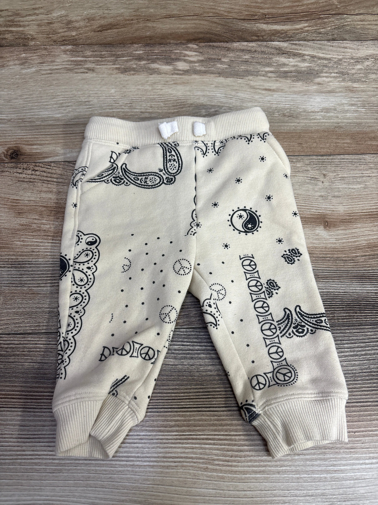 Cream baby pants with black bandana print, peace signs, and ribbed cuffs on wooden surface