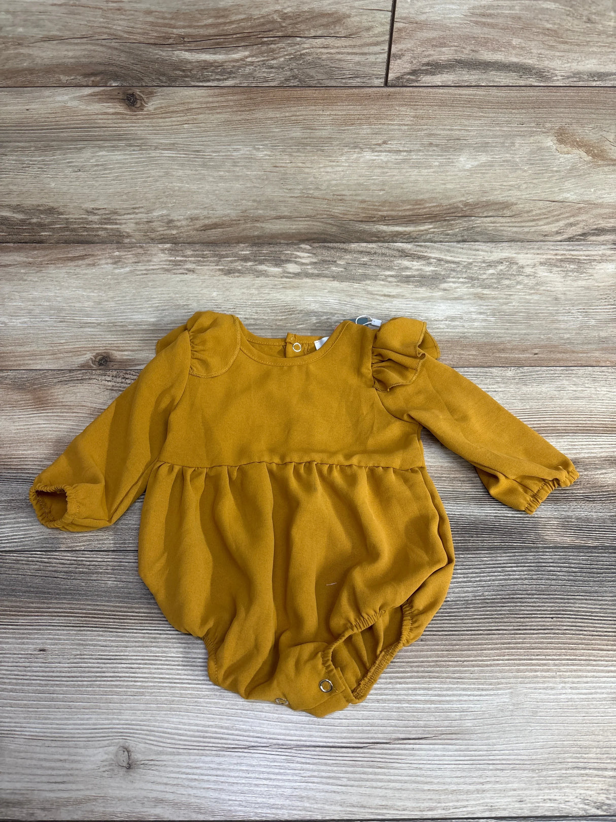 Mustard yellow baby romper with long sleeves and snaps, displayed on wood background
